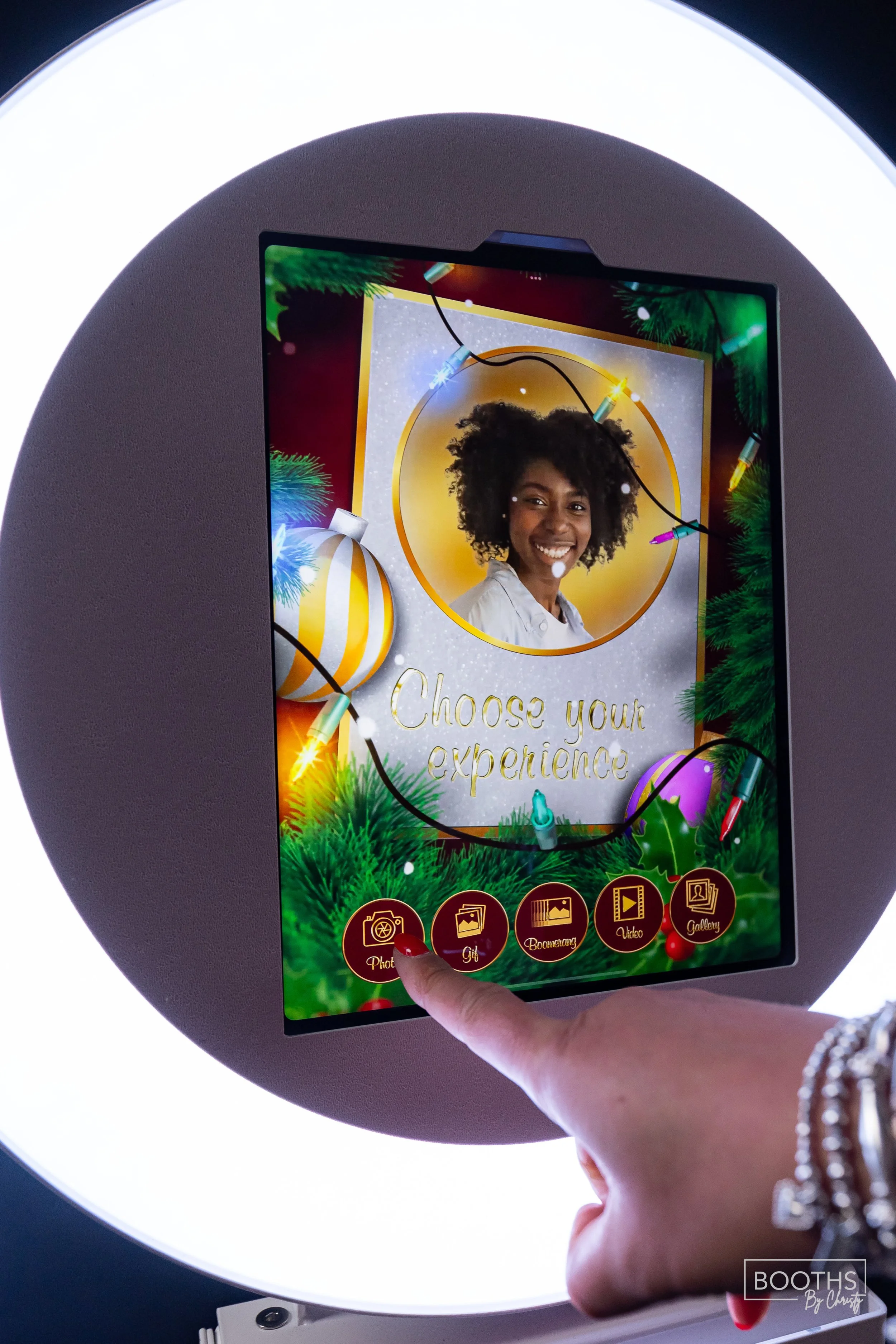 A photo booth touchscreen displaying a holiday-themed interface with a woman's photo and the message 'Choose your experience'. The screen shows options for Photo, Gif, Boomerang, Video, and Gallery at the bottom.