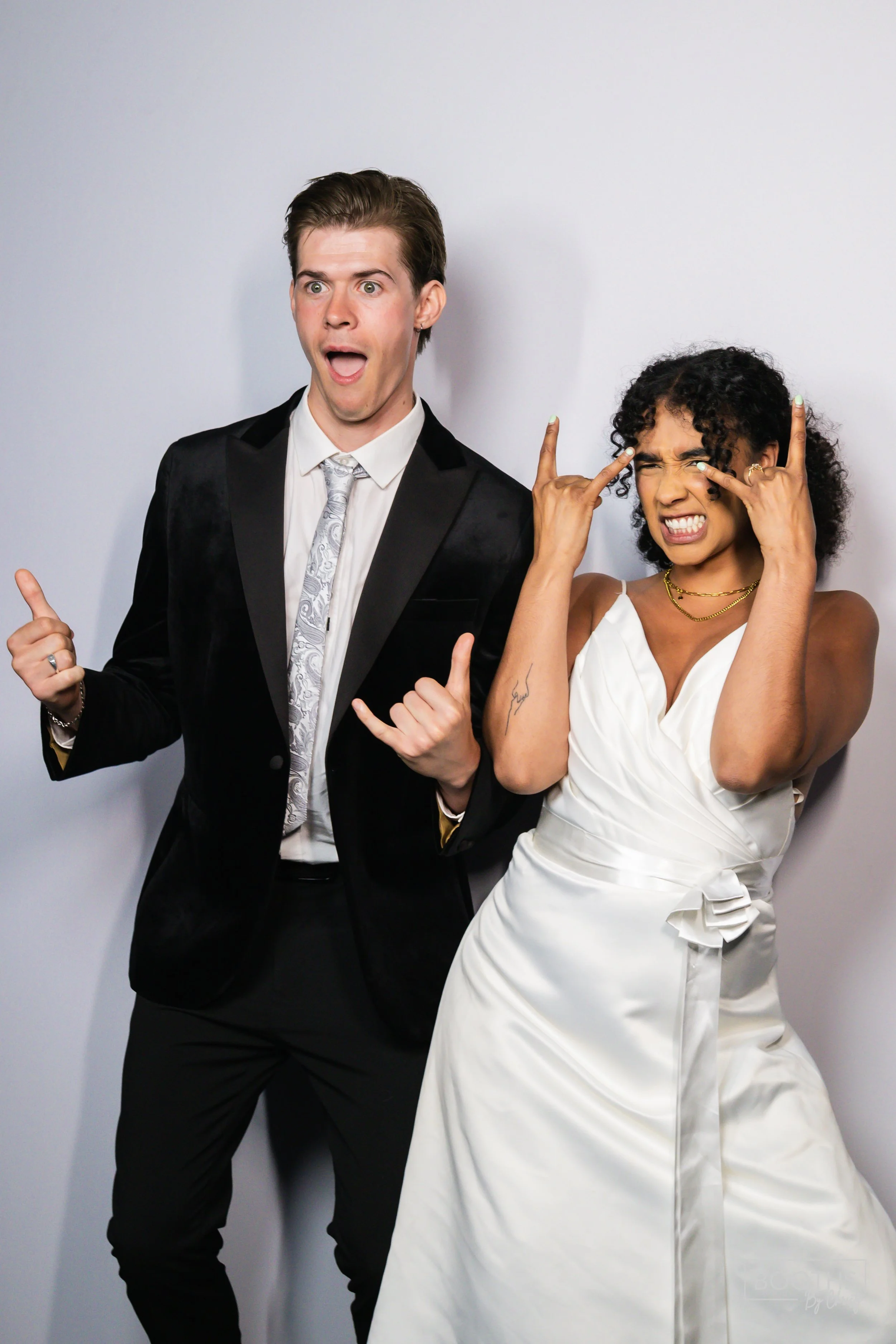 A man and woman dressed in formal attire making humorous gestures and facial expressions against a plain white background.