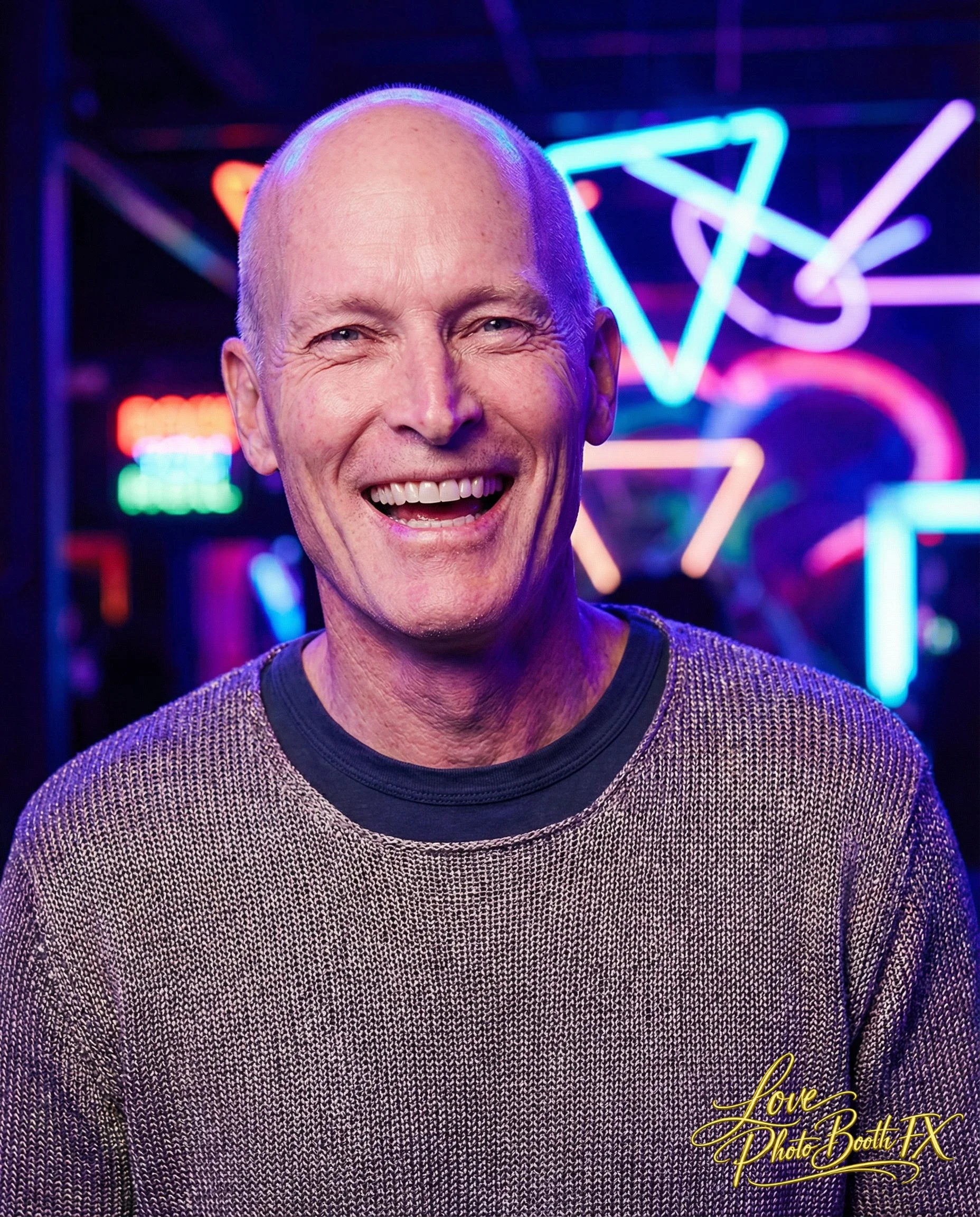 A man smiling broadly in front of a background with colorful neon lights.