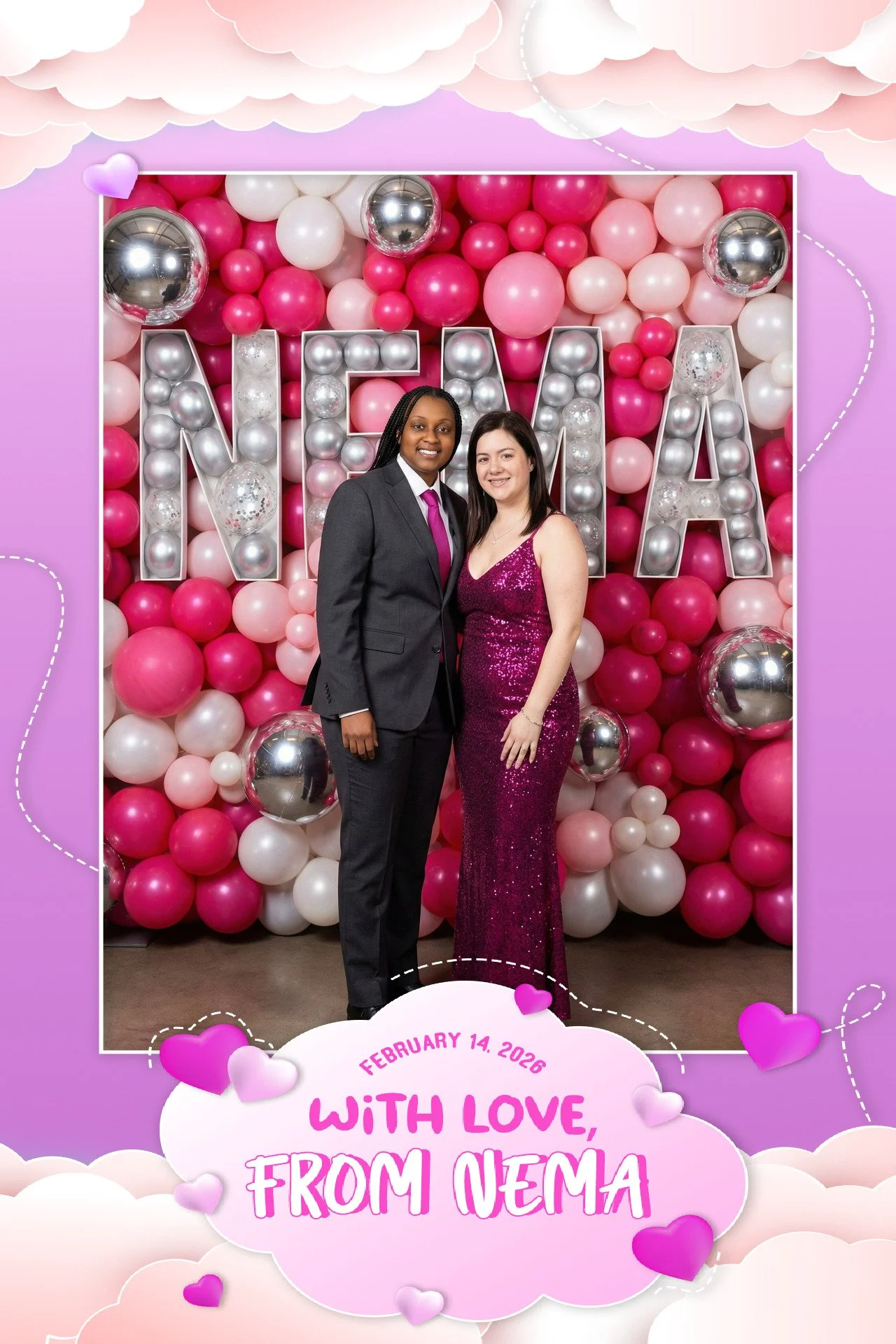 Two women standing in front of a pink, white, and silver balloon backdrop with large letter balloons spelling 'MAMA.' One woman is dressed in a dark suit with a pink tie, and the other is wearing a sparkly pink dress. The image has a decorative borde