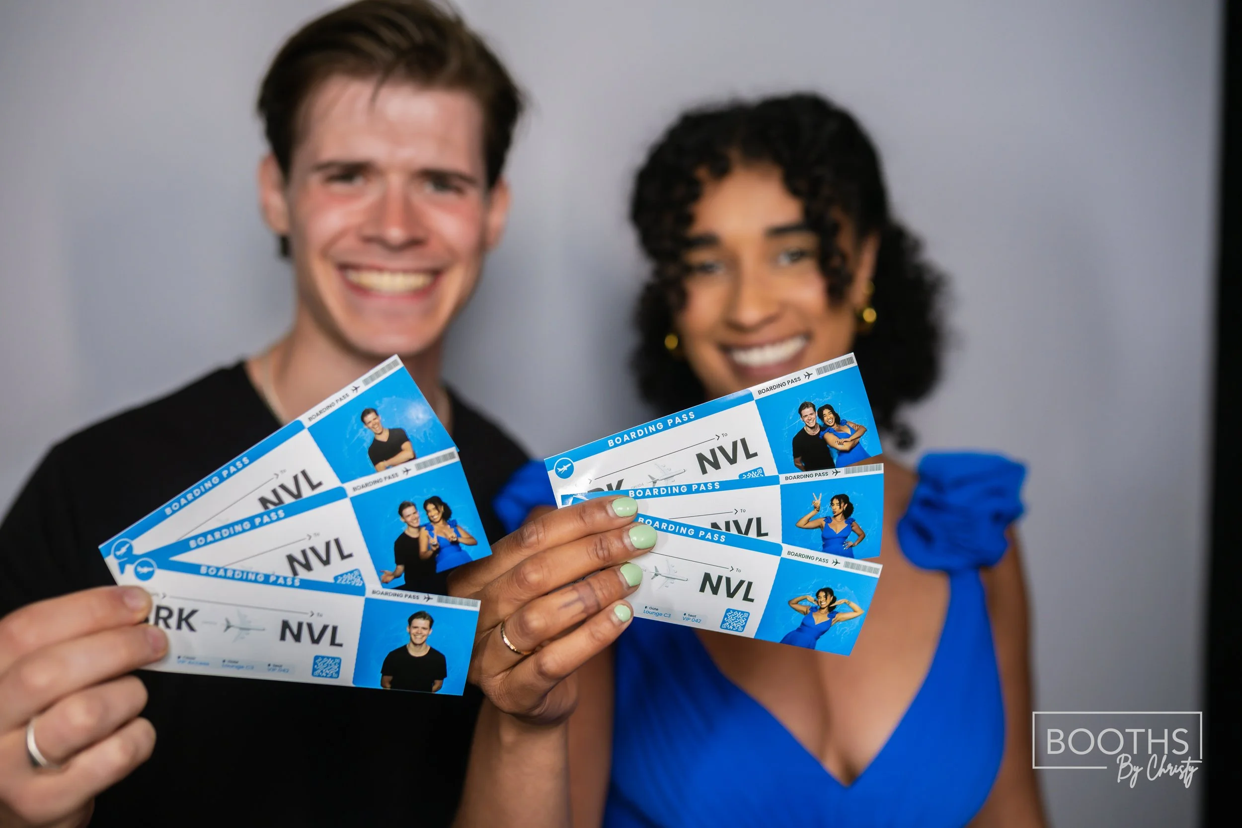 Two excited people holding airline boarding passes, smiling for the camera. The man is wearing a black shirt, and the woman is in a blue dress with ruffled sleeves.