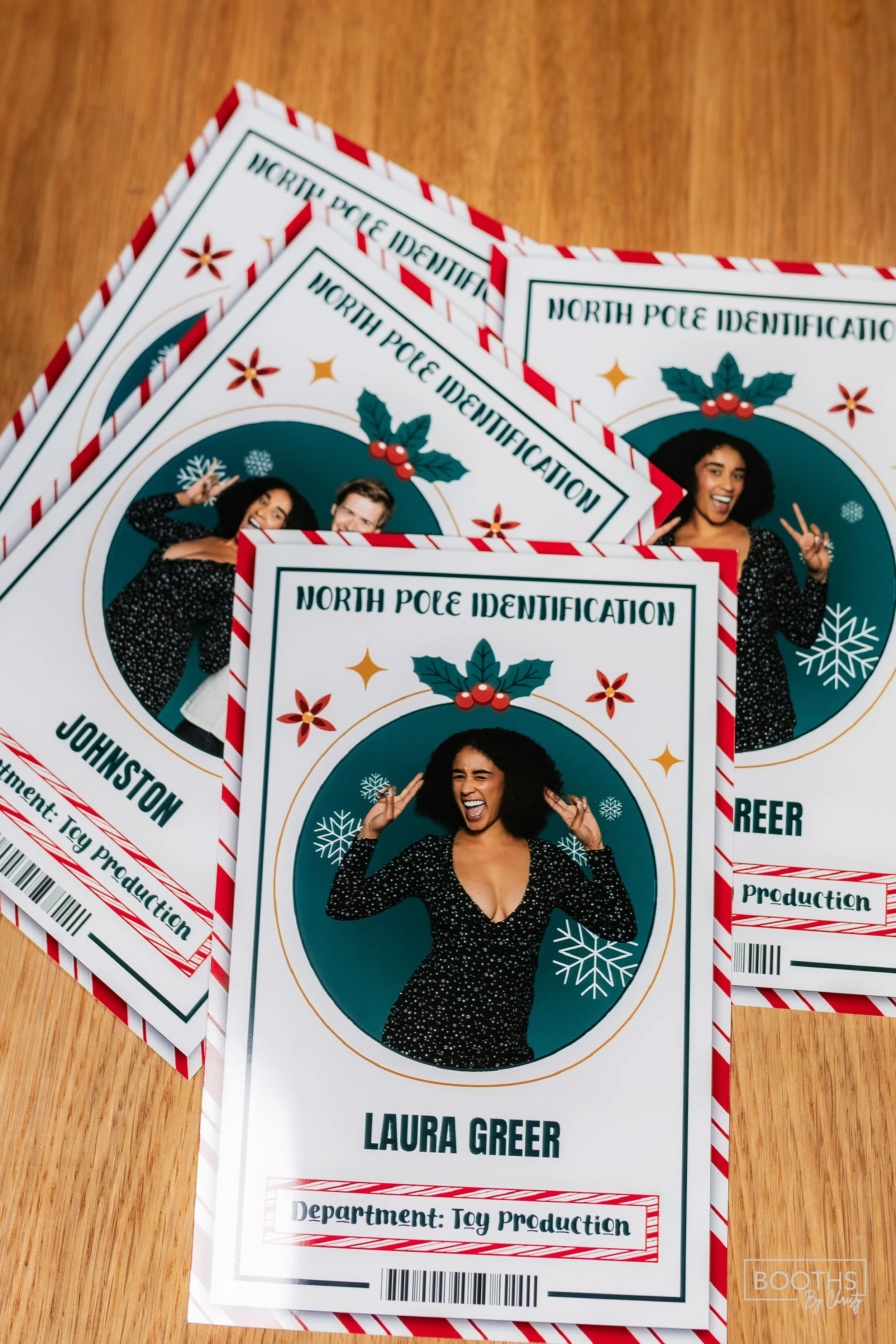 Holiday-themed ID badges for North Pole Identification featuring a woman with curly hair, in a black dress with white dots, smiling and making peace signs, decorated with snowflakes and holly berries. One badge is labeled 'Laura Greer' from the Toy P