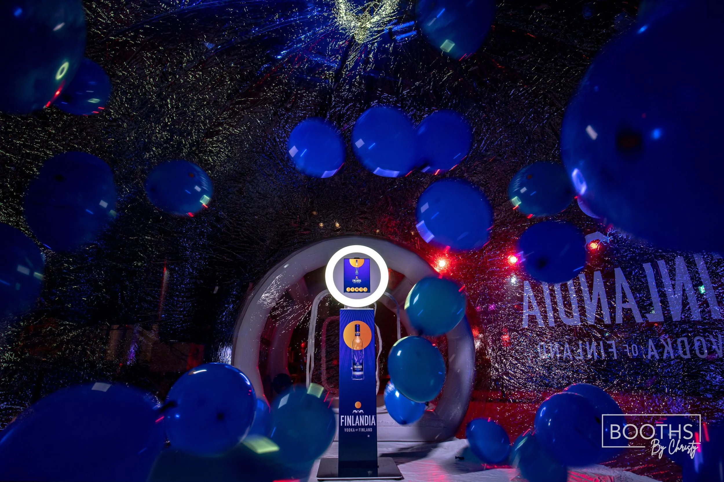 Display with blue balloons and promotional stand for Finlandia Vodka inside a reflective, metallic, tunnel-like structure with red and blue lighting.