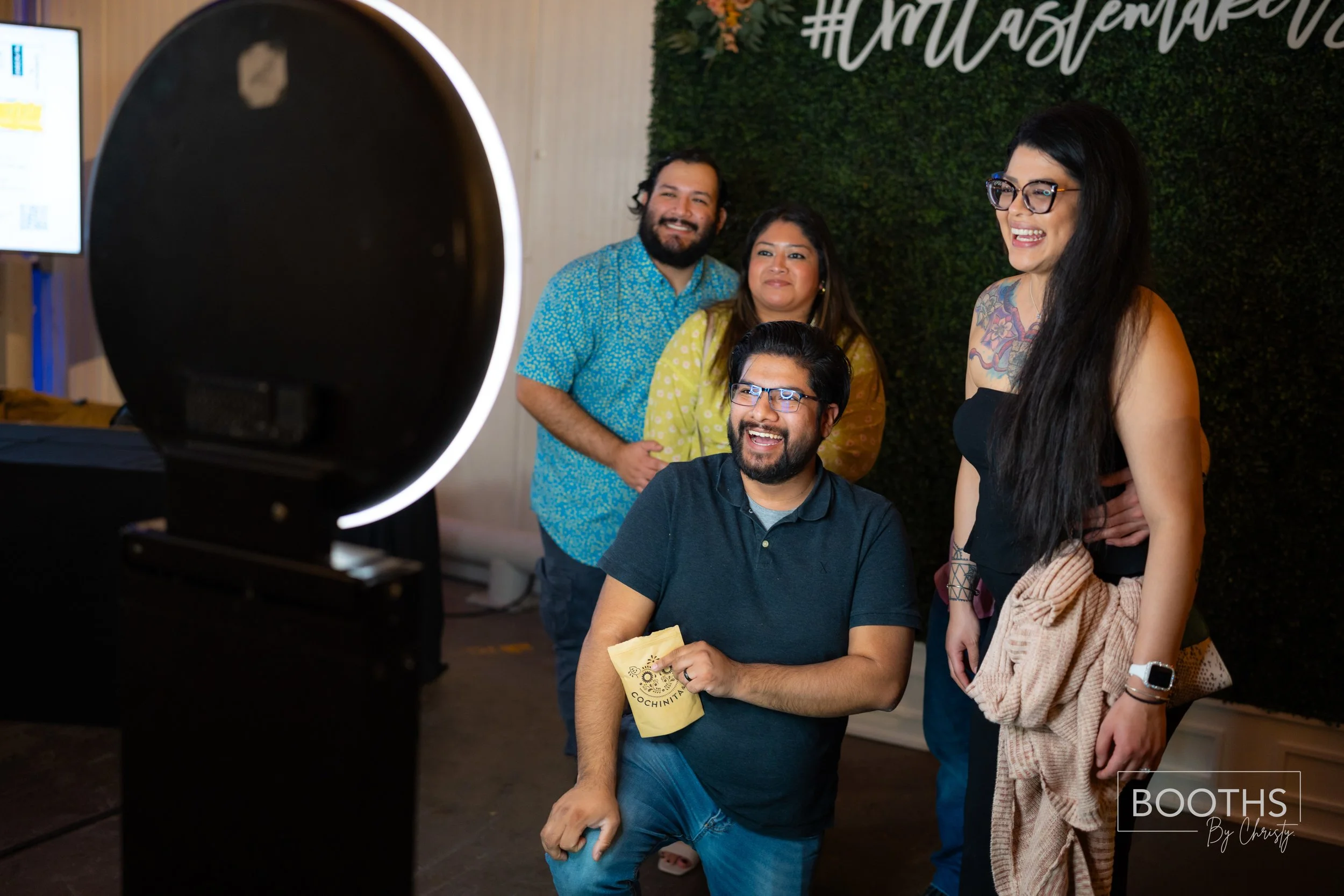 Four diverse friends are taking a photo using a circular ring light in a decorated indoor setting, smiling and enjoying themselves.