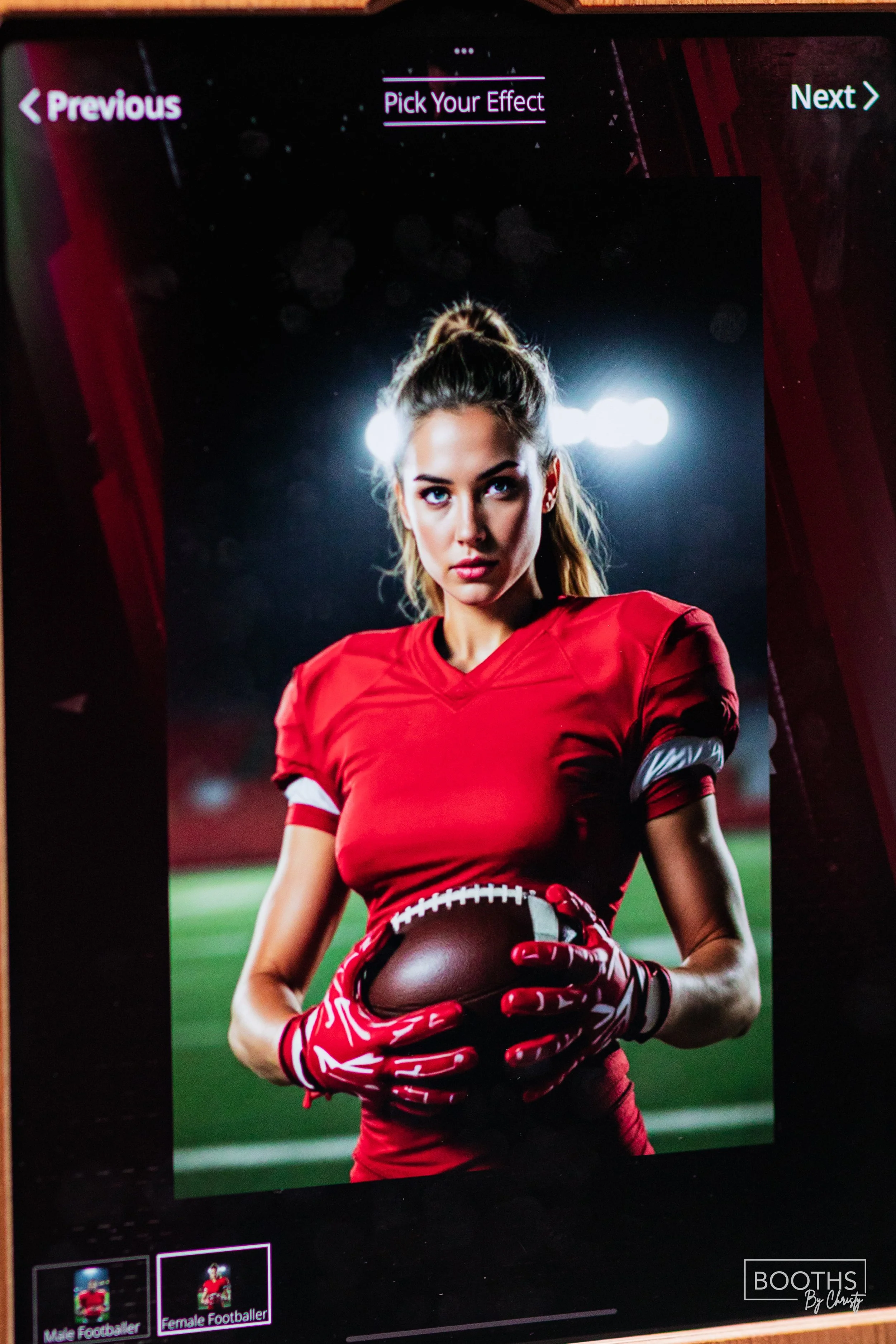 A female football player in a red uniform holding a football, standing on a field at night with bright stadium lights in the background.