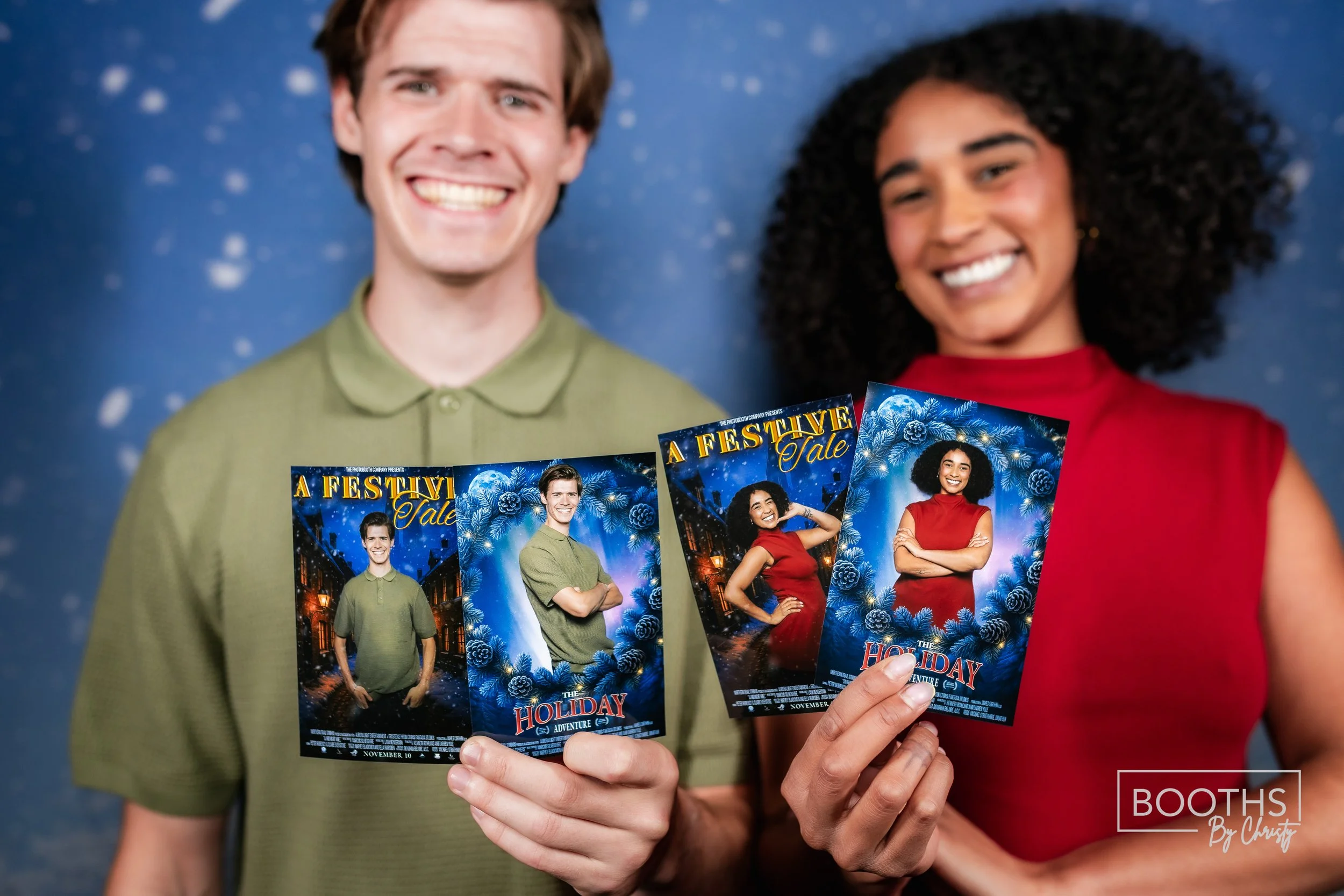 A man and woman smiling while holding holiday-themed photo booth cards with festive blue and red designs, featuring the text 'A Festive Tale' and 'The Holiday Adventure'.