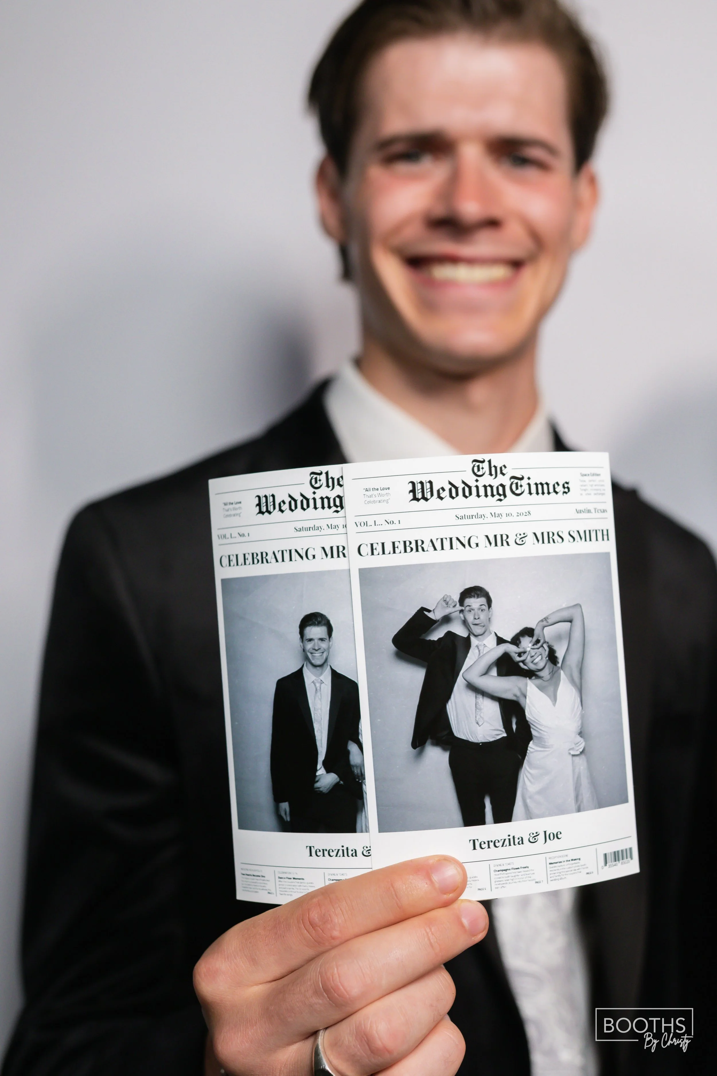A man in a tuxedo holding two black-and-white wedding newspapers that feature photos of the couple, smiling and making playful gestures.