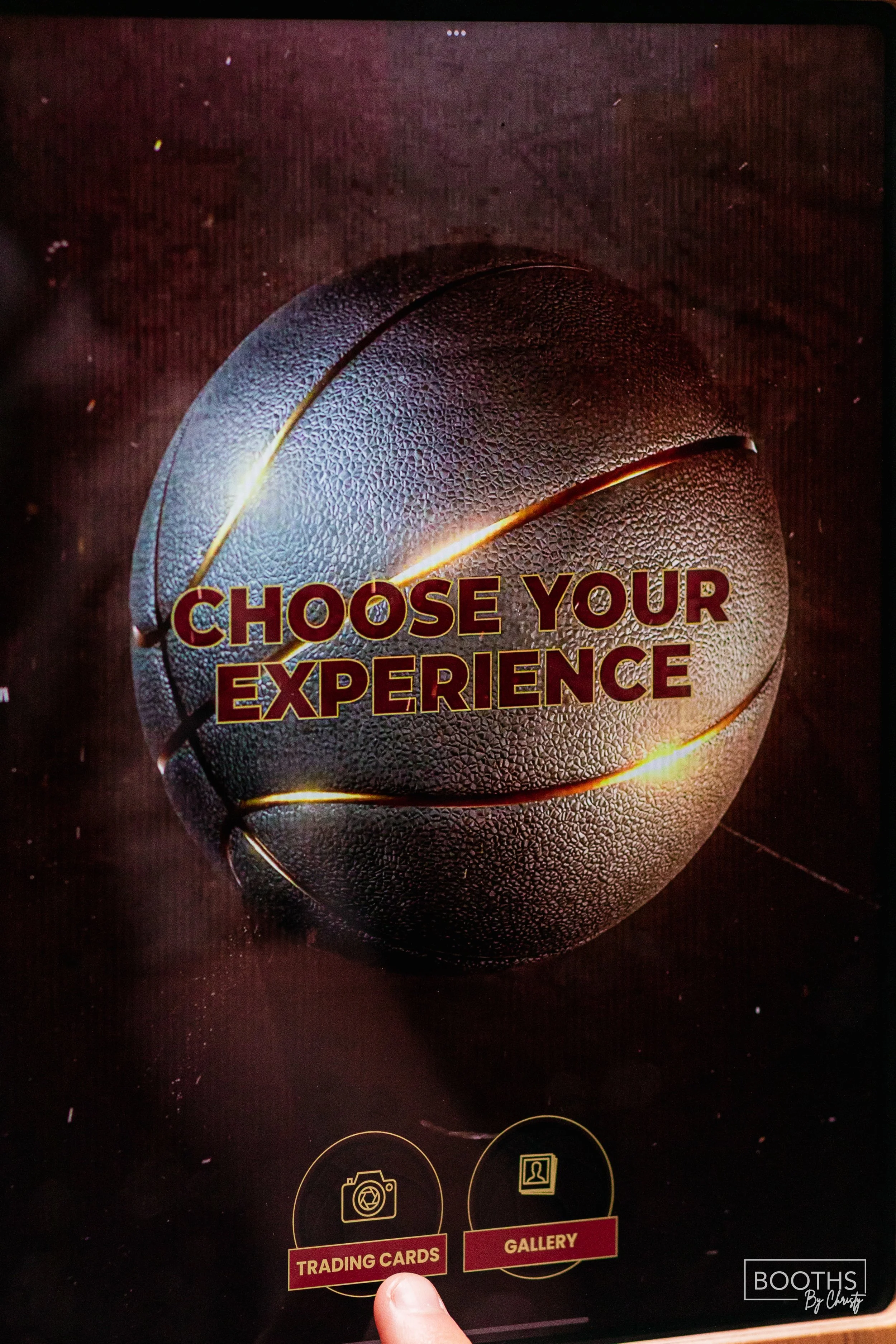 A digital screen displaying a large textured basketball with the text "Choose Your Experience" across it. Below, there are icons and labels for "Trading Cards" and "Gallery."