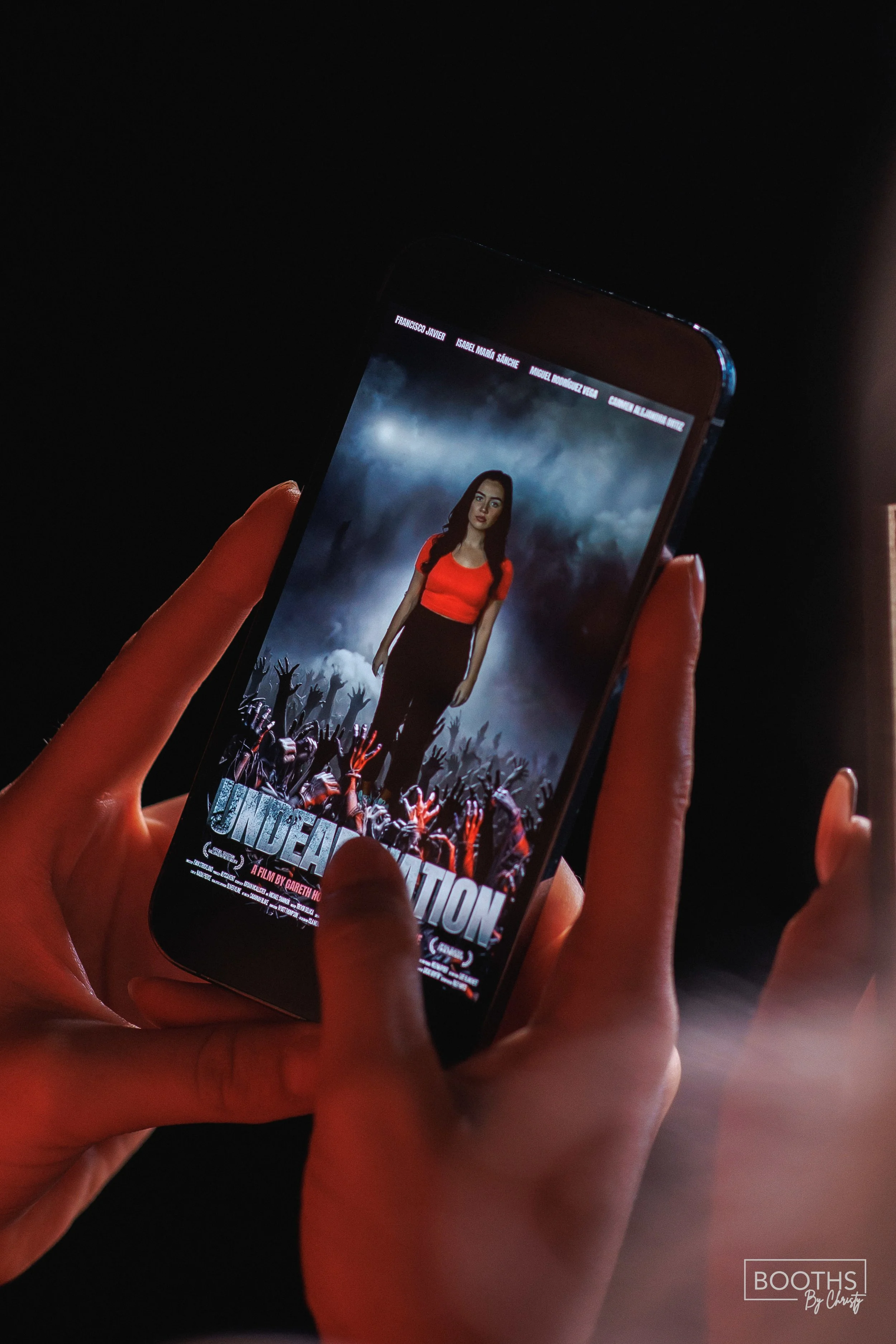 Person holding a smartphone displaying a movie poster for "Undeviated" featuring a woman in a red top against a dark, stormy crowd background.