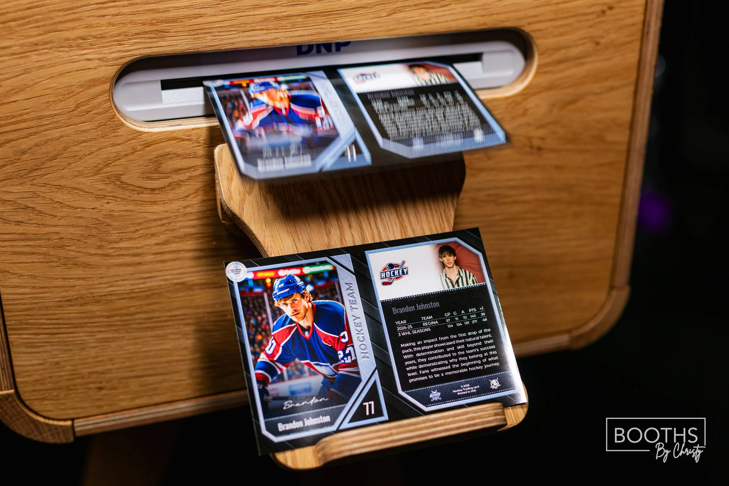 Hockey trading card being dispensed from a wooden booth, featuring a player in a blue and red uniform, with additional card showing player statistics and a portrait.