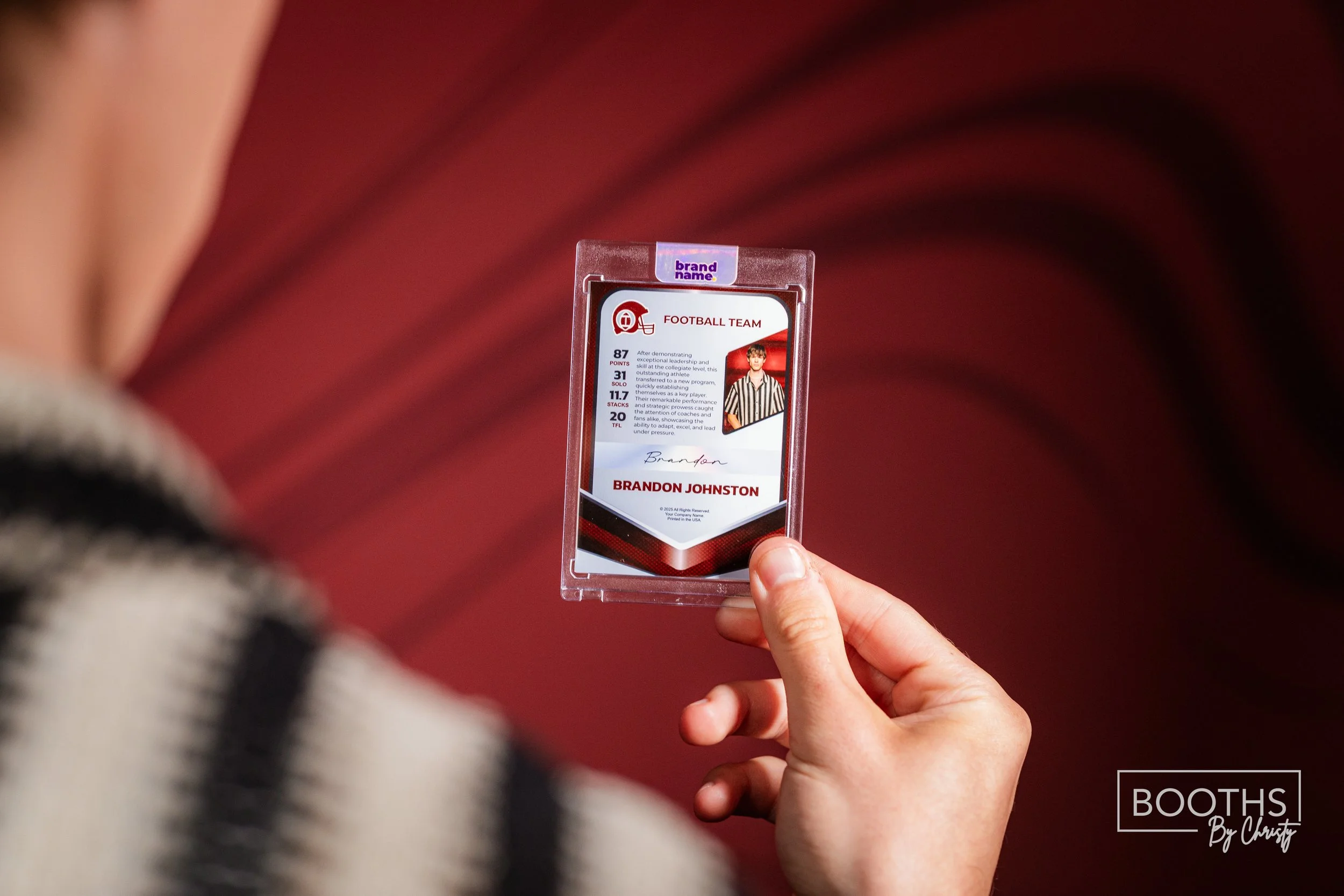 Hand holding a sports ID badge featuring a football team, player's name Brandon Johnston, and statistics, in a protective plastic case with a maroon background.