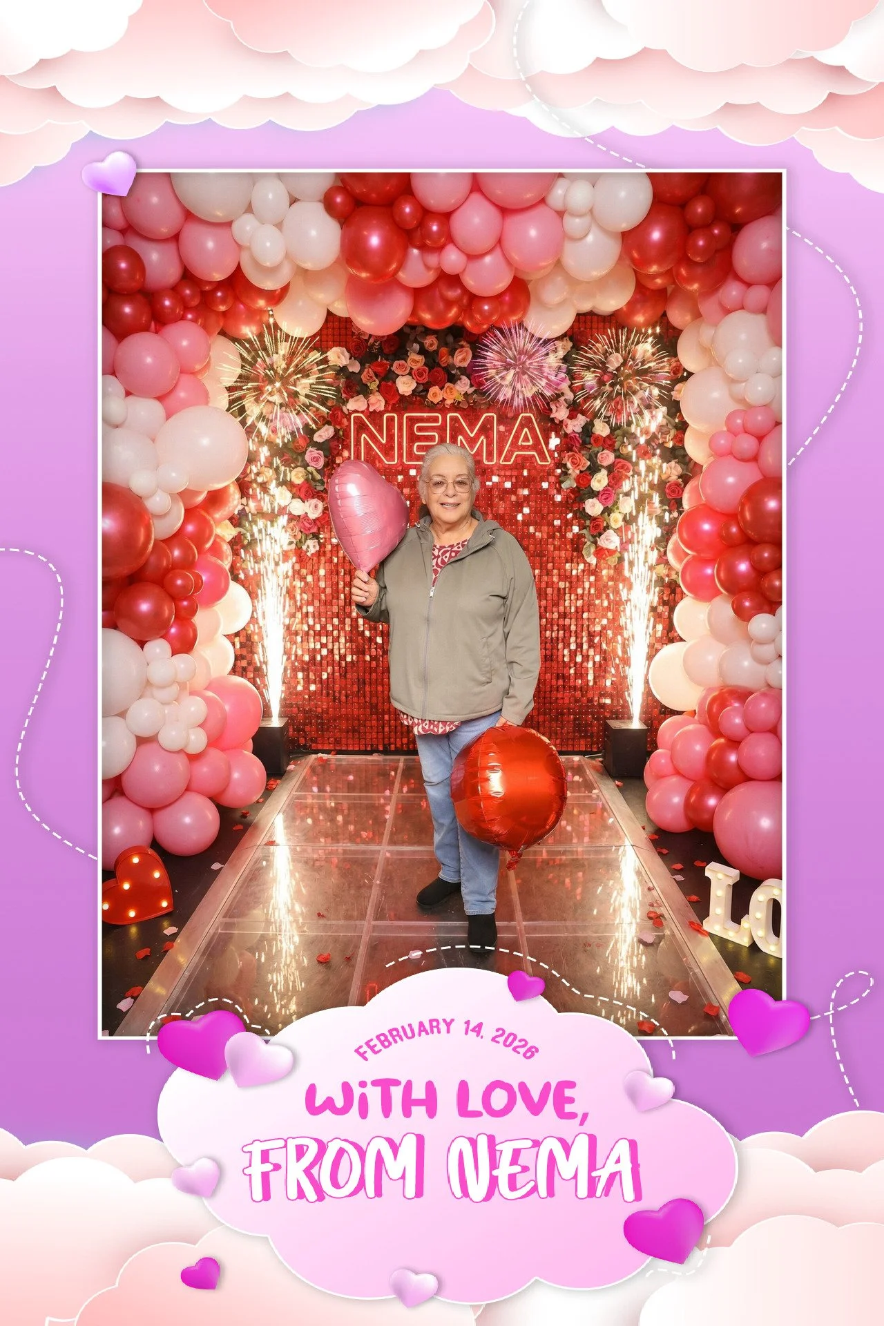 A smiling elderly woman holding pink and red heart-shaped balloons stands in a festive Valentine's Day decorated setting. The background features red sequins, balloons, and fireworks, with the name 'NEMA' illuminated in neon lights.