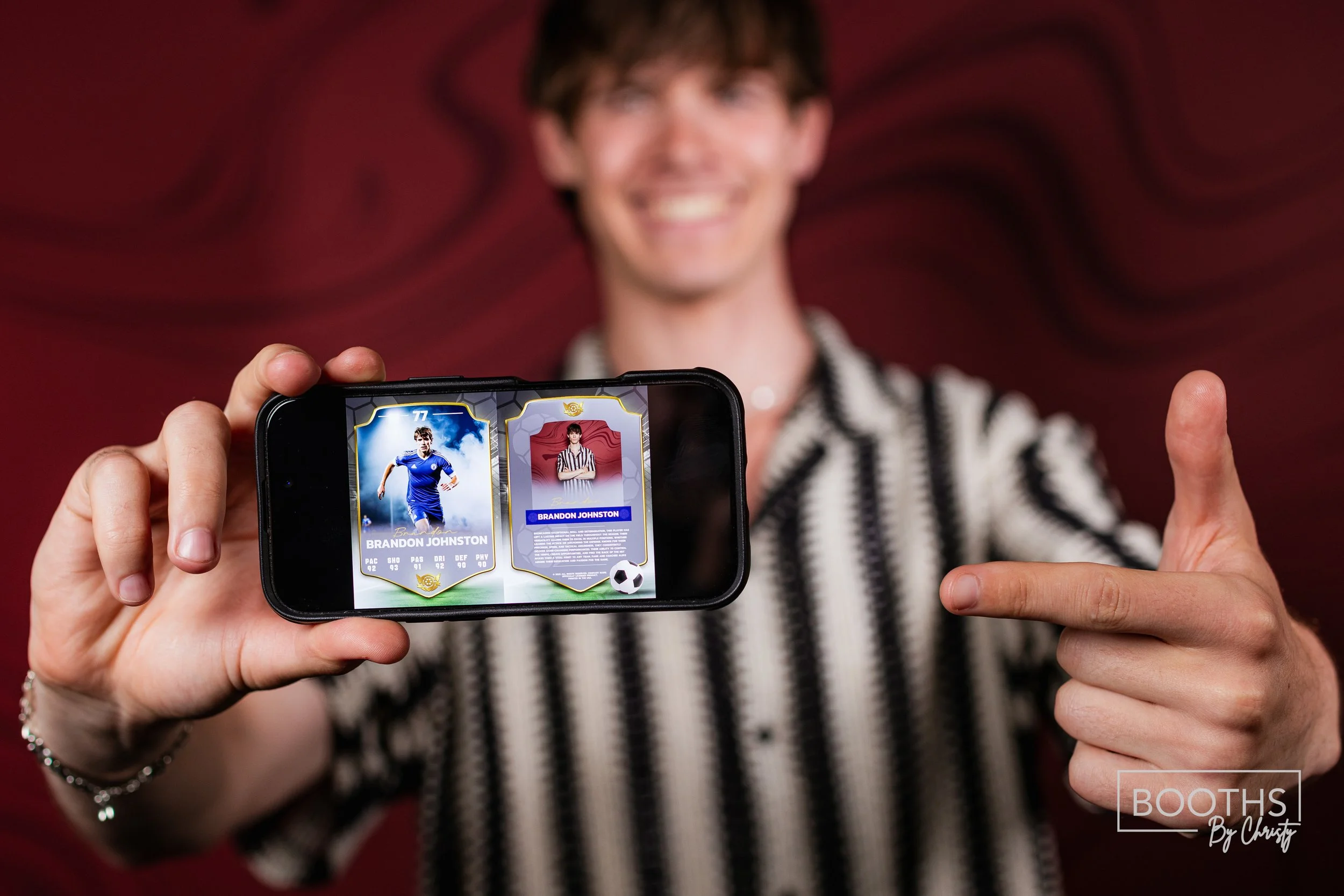 A person with a striped shirt points to a phone displaying virtual trading cards of a soccer player named Brandon Johnston. The background is red.