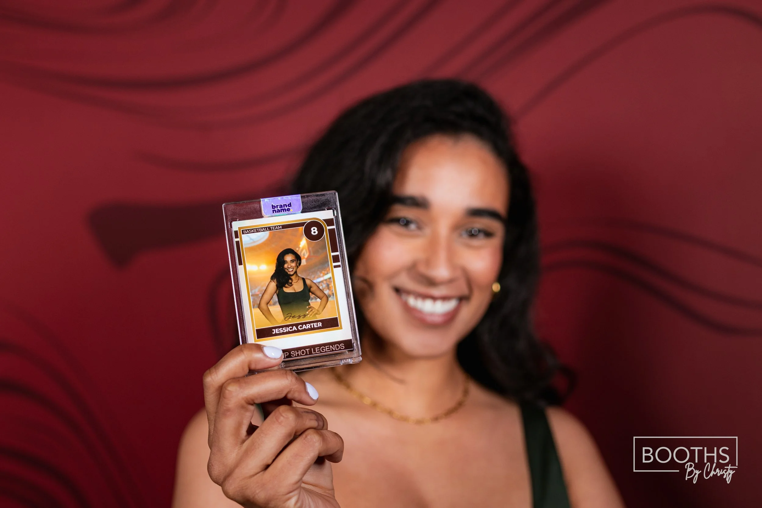 A woman smiling and holding up a card with her portrait, name Jessica Carter, and her team number at a sports event, against a red background with wavy black lines.