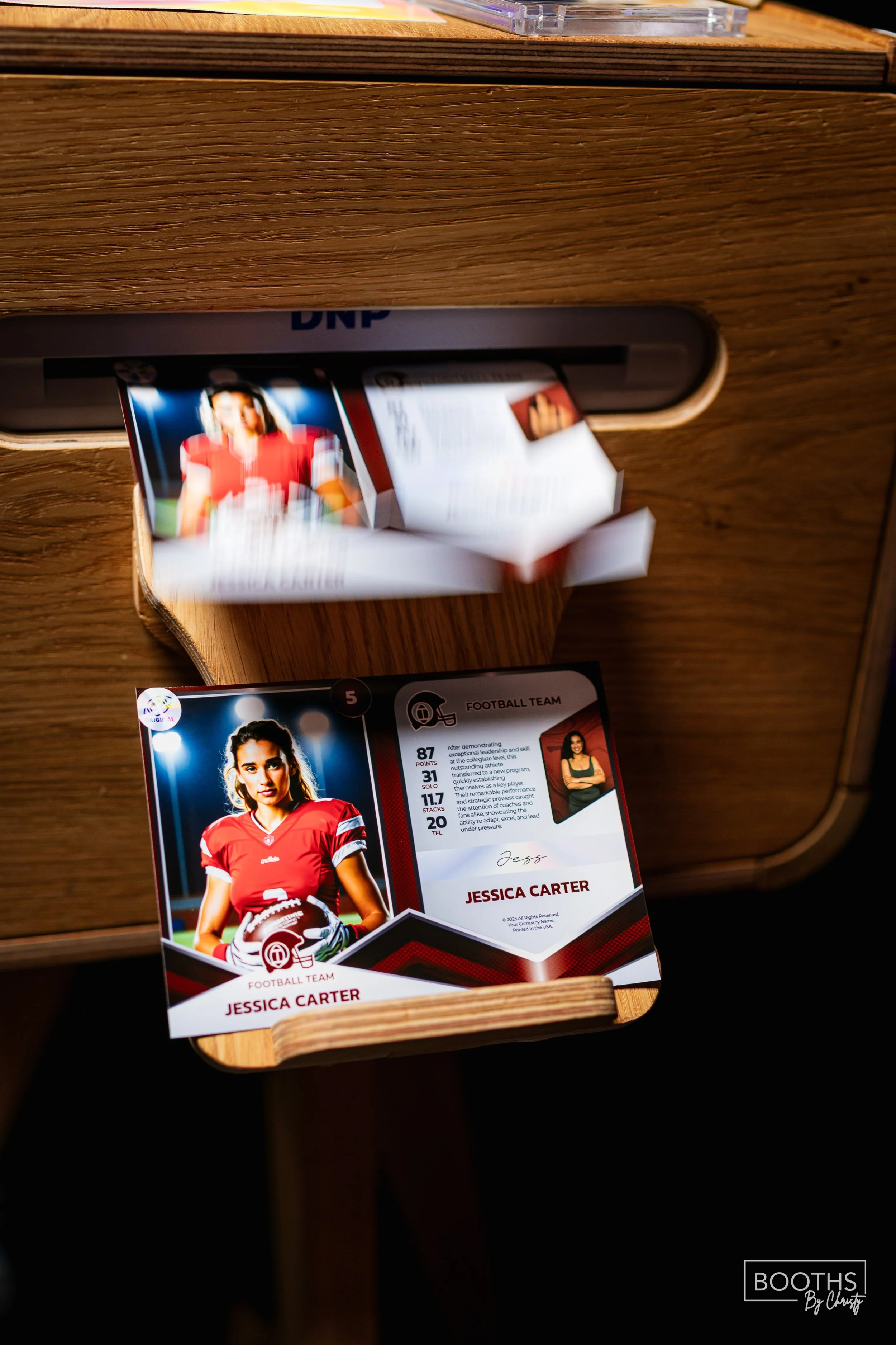 A football trading card for Jessica Carter, a female football player, sitting on a wooden surface. The card features her wearing a red football jersey and holding a football, with her name and stats printed on it.