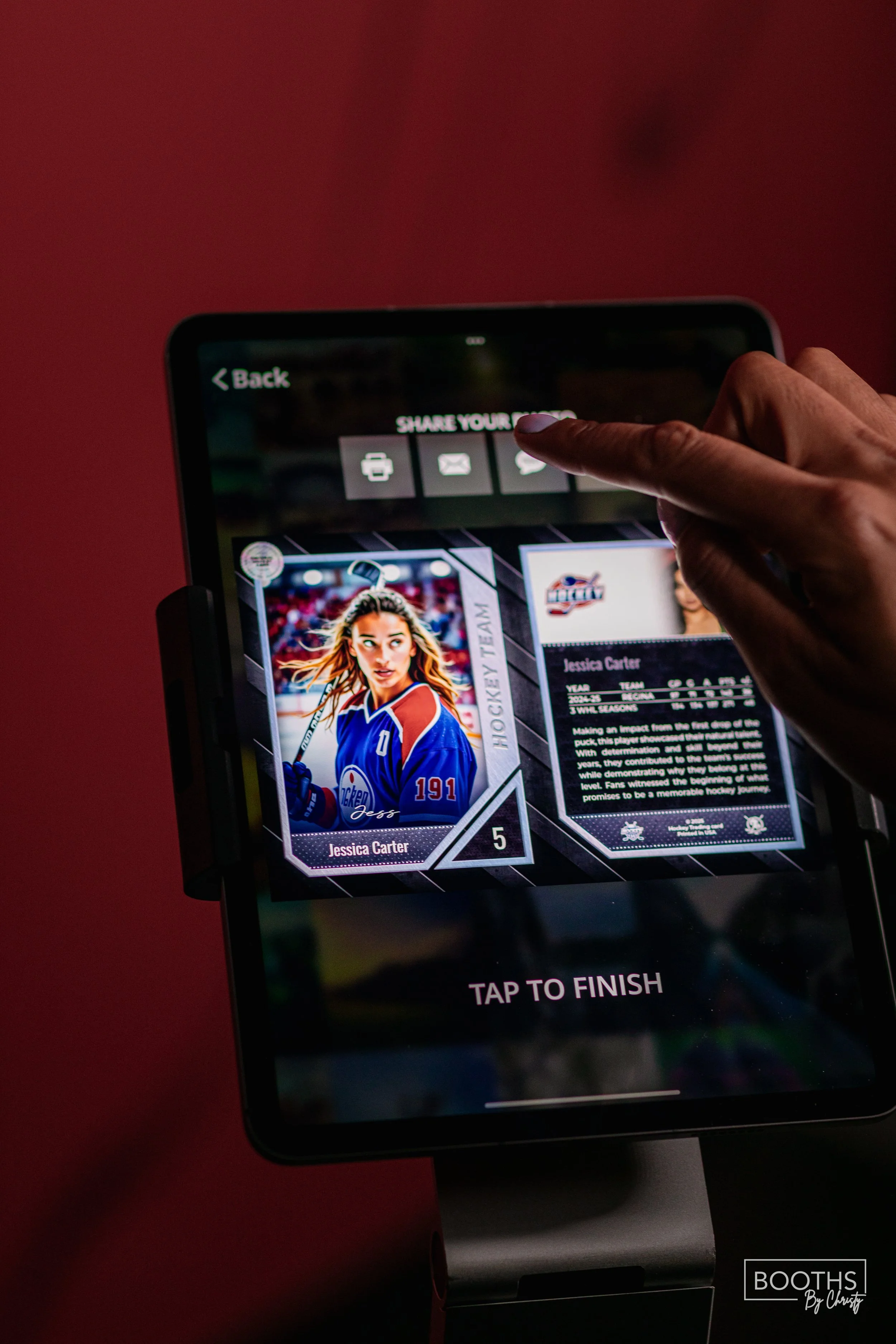 A person interacts with a touchscreen device displaying a digital hockey trading card of Jessica Carter, wearing a blue hockey jersey, with options to share the card via various apps.