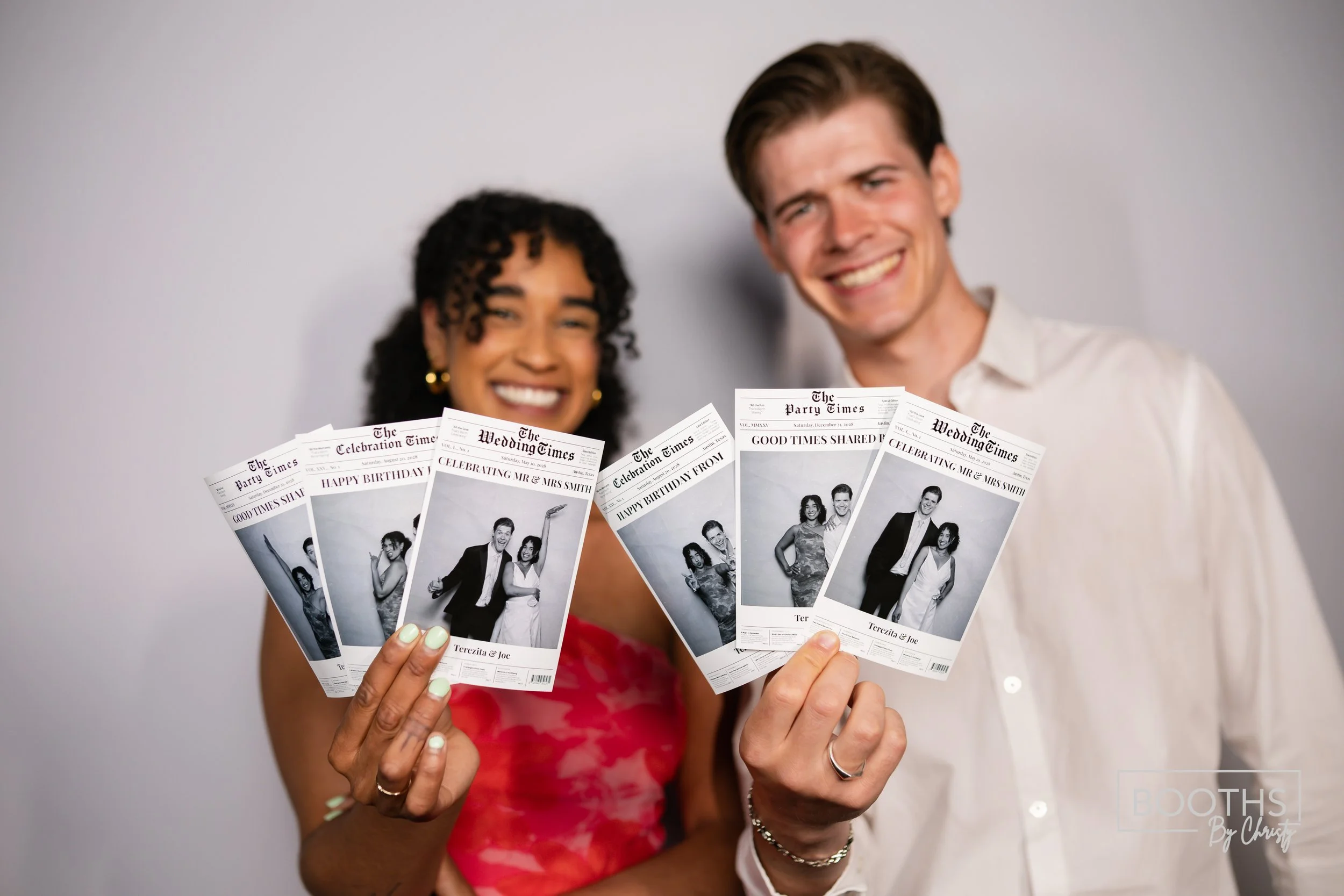 Smiling woman and man holding four black and white wedding or event program booklets with photographs of a couple on the front.