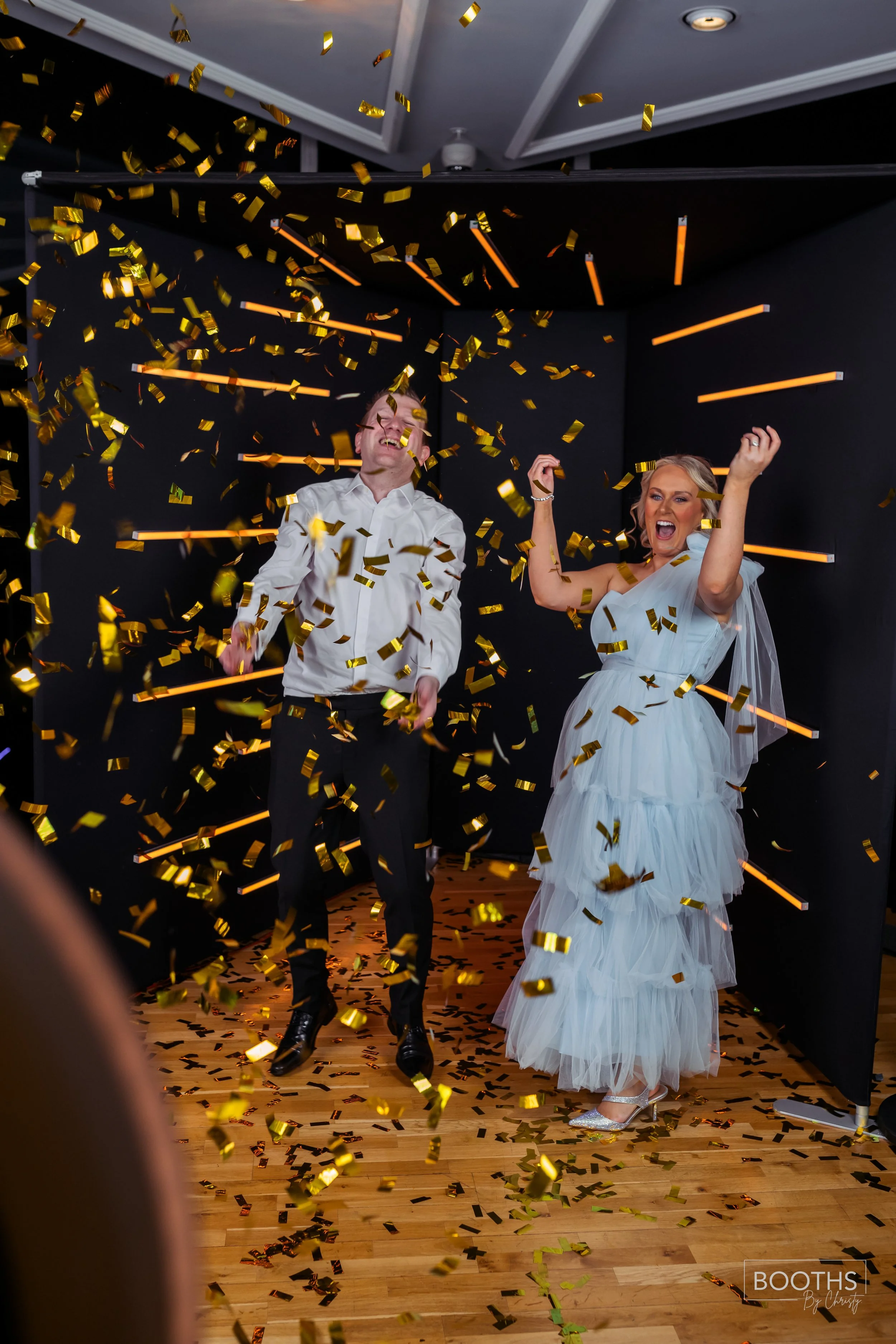 A bride and groom celebrating as gold confetti falls around them at their wedding reception.