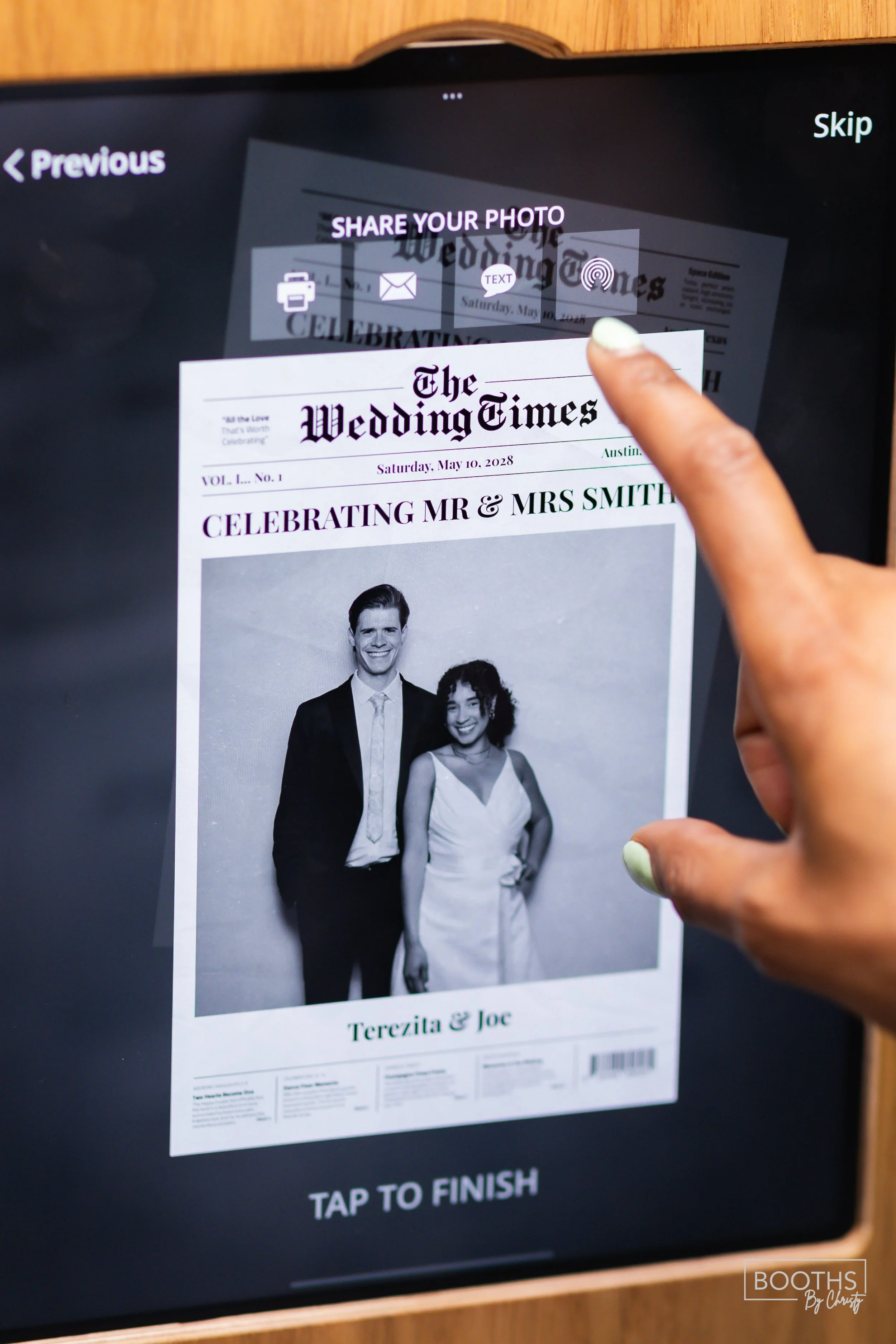 A person using a touchscreen device to share a black and white photo of a wedding. The photo features a man in a dark suit and a woman in a white dress, standing side by side. The device screen displays options to share via printer, email, text, or f