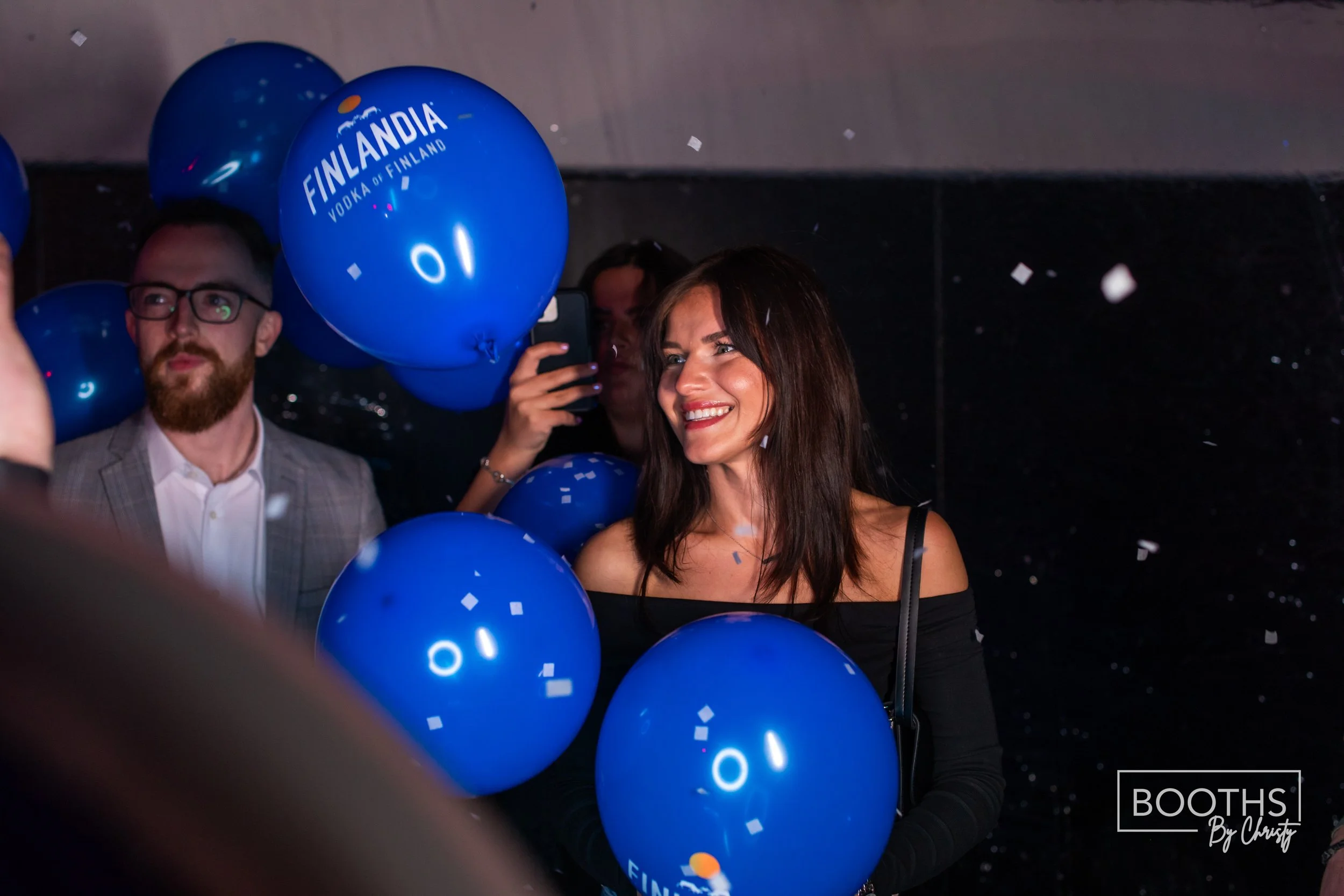 Smiling woman holding blue balloons with 'Finlandia Vodka' written on them at a celebration event.