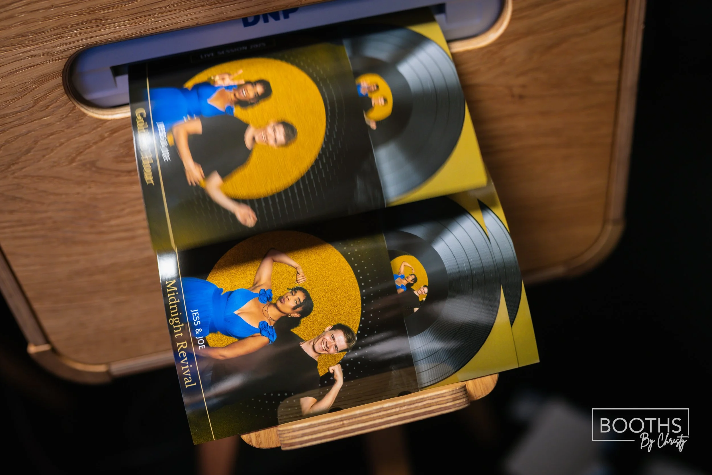 Promotional flyers for a musical event titled 'Midnight Revival' featuring JESS & JOE, with a photo of Jess and Joe, set against black vinyl records and a yellow background, displayed on a wooden surface.