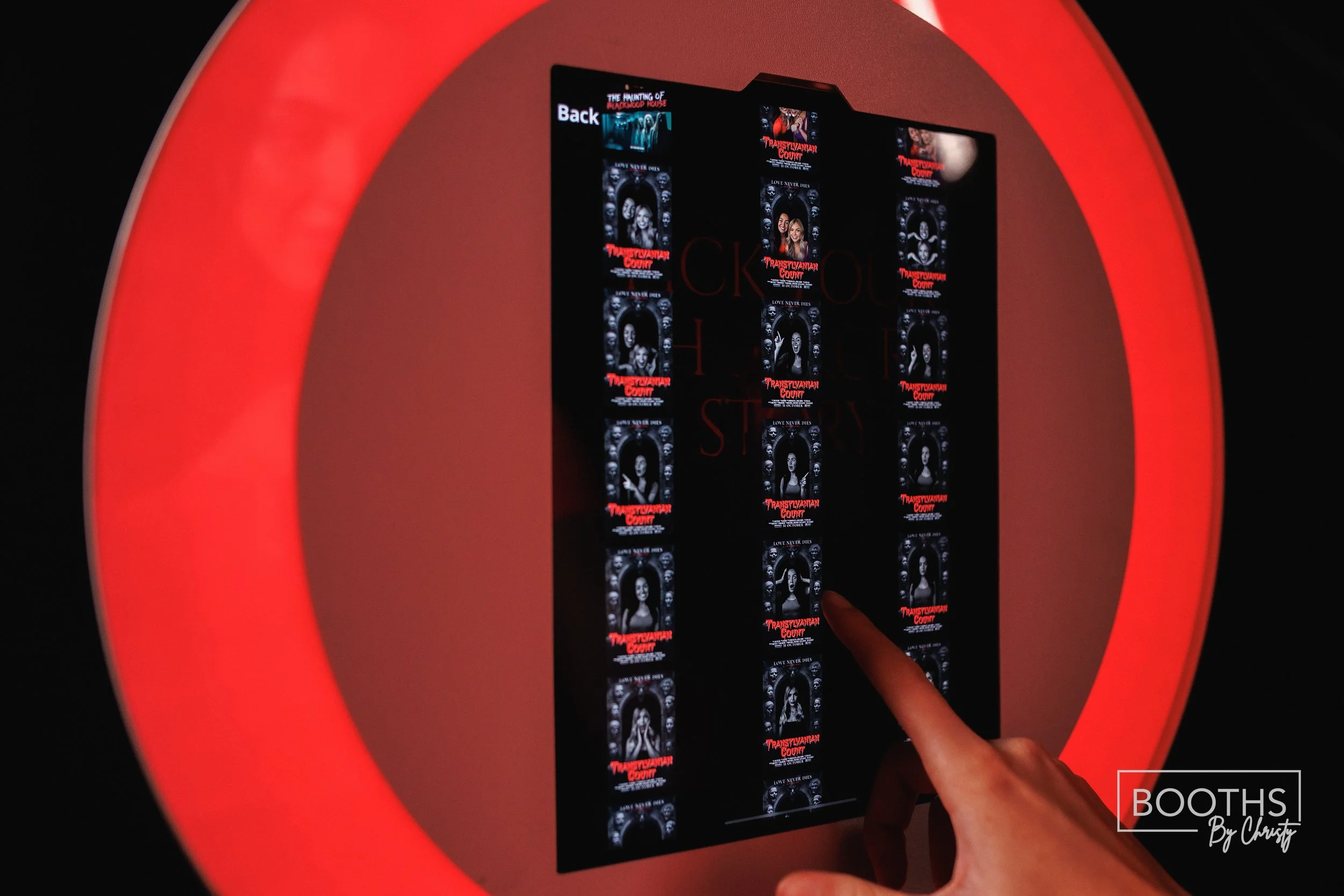 A person is selecting a movie ticket from a digital kiosk displaying posters for the movie 'Transylvania Count' with a red glow around the screen.