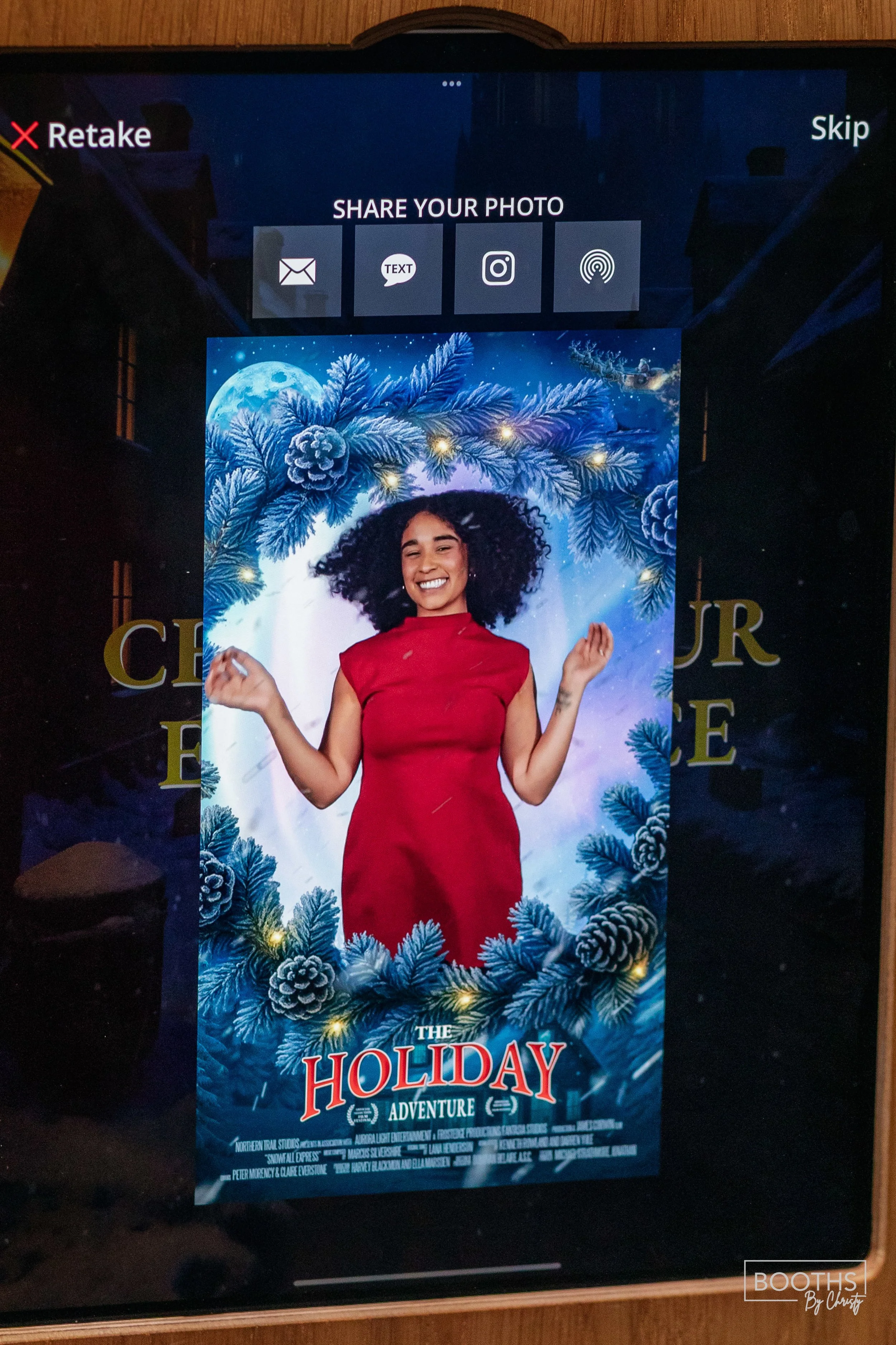 Digital photo booth screen displaying a festive holiday poster featuring a woman with curly hair in a red dress, surrounded by pine branches, pinecones, and Christmas lights. The poster is titled "The Holiday Adventure."