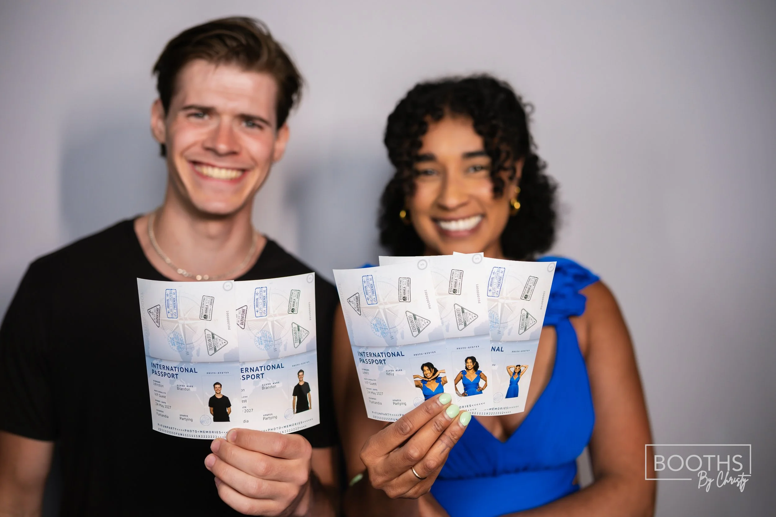 Two smiling people holding up passports with boarding passes in front of a plain wall.
