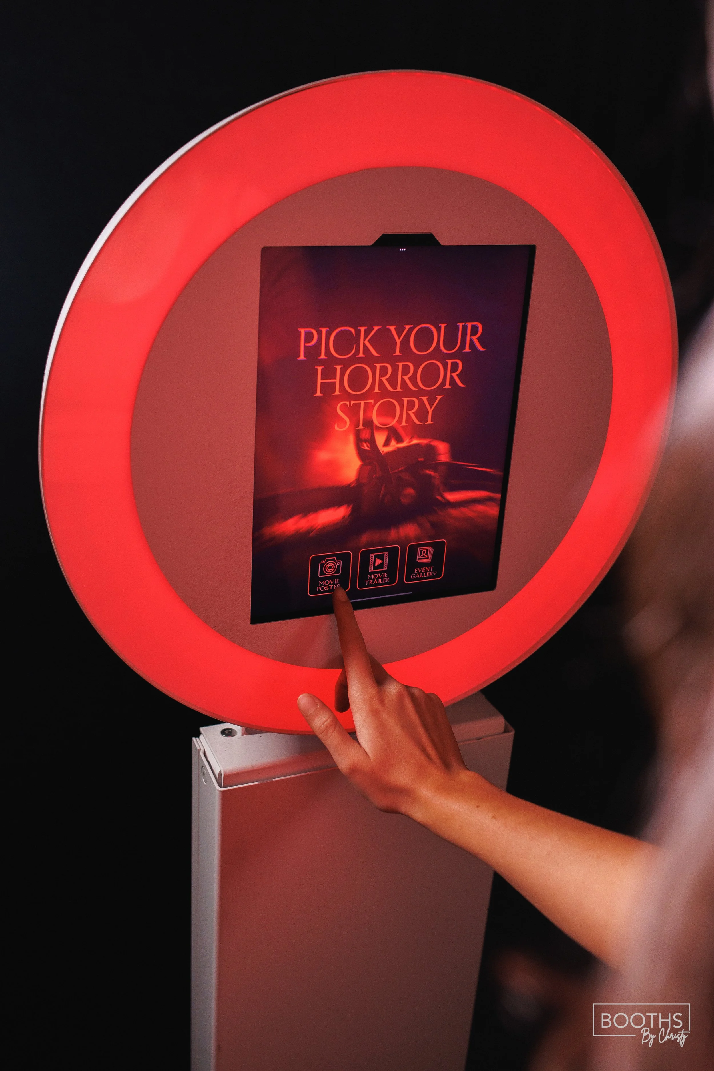 Interactive digital display screen with red neon lighting border, inviting users to pick their horror story, with icons for movie poster, trailer, and event gallery.