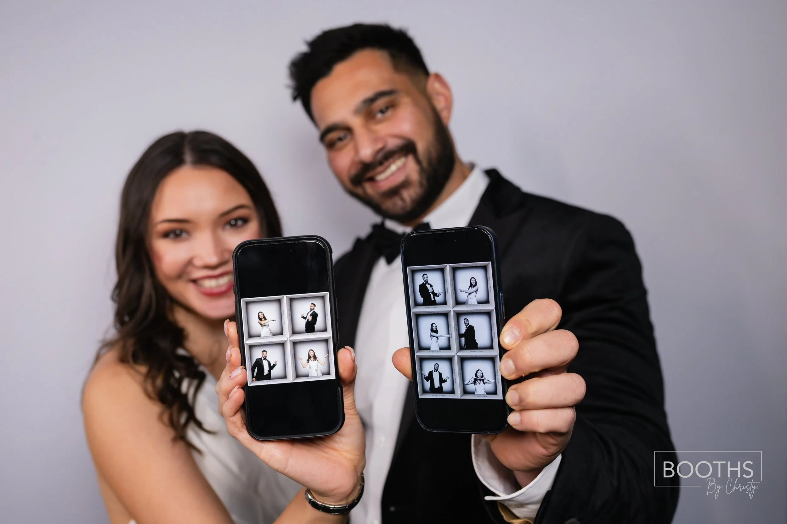A couple in formal attire holding smartphones with photo booth images of themselves and smiling at the camera.