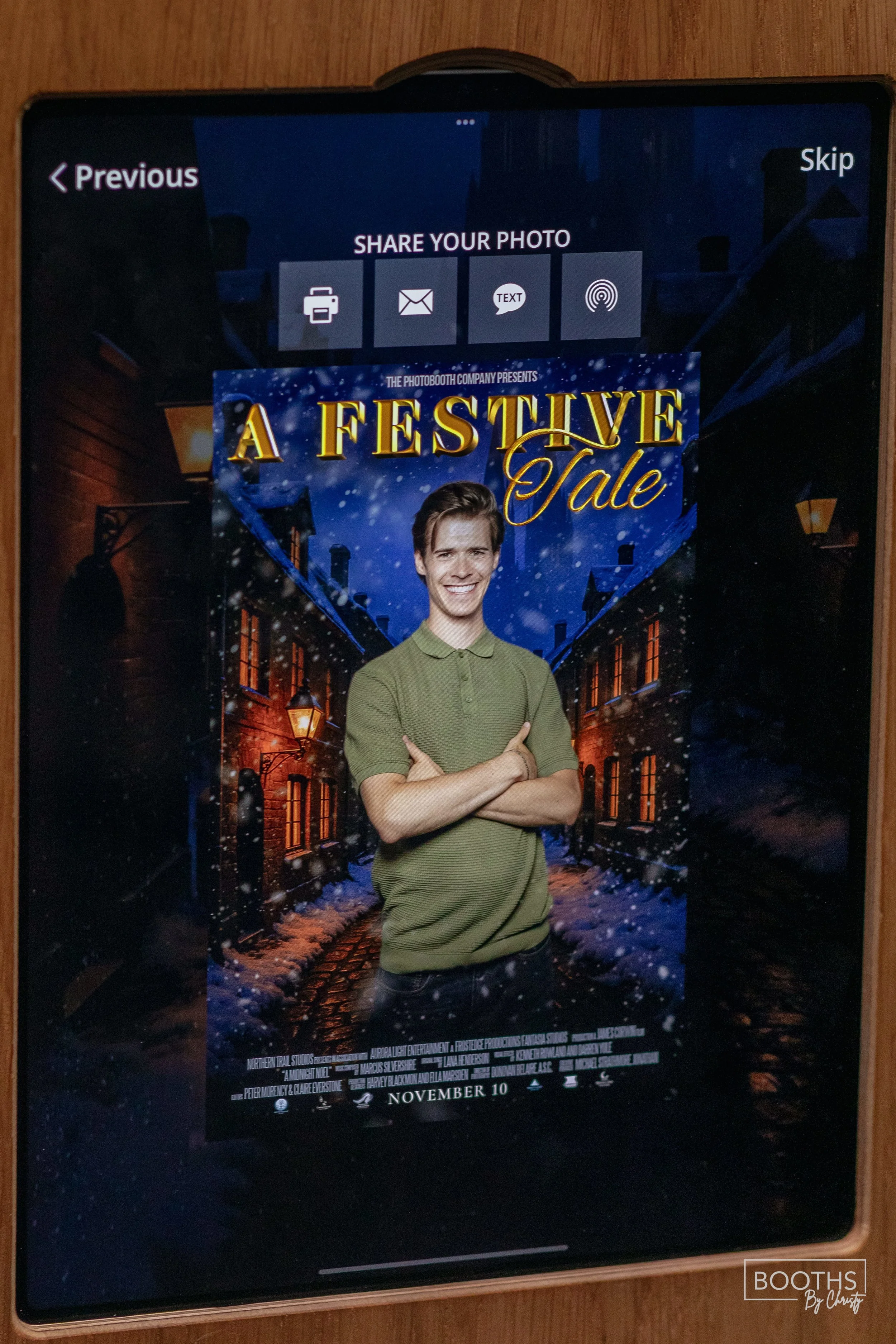 Digital screen displaying a promotional poster for a movie titled 'A Festive Tale' with a smiling young man in a green shirt standing with crossed arms in front of a festive, snow-covered street scene at night.