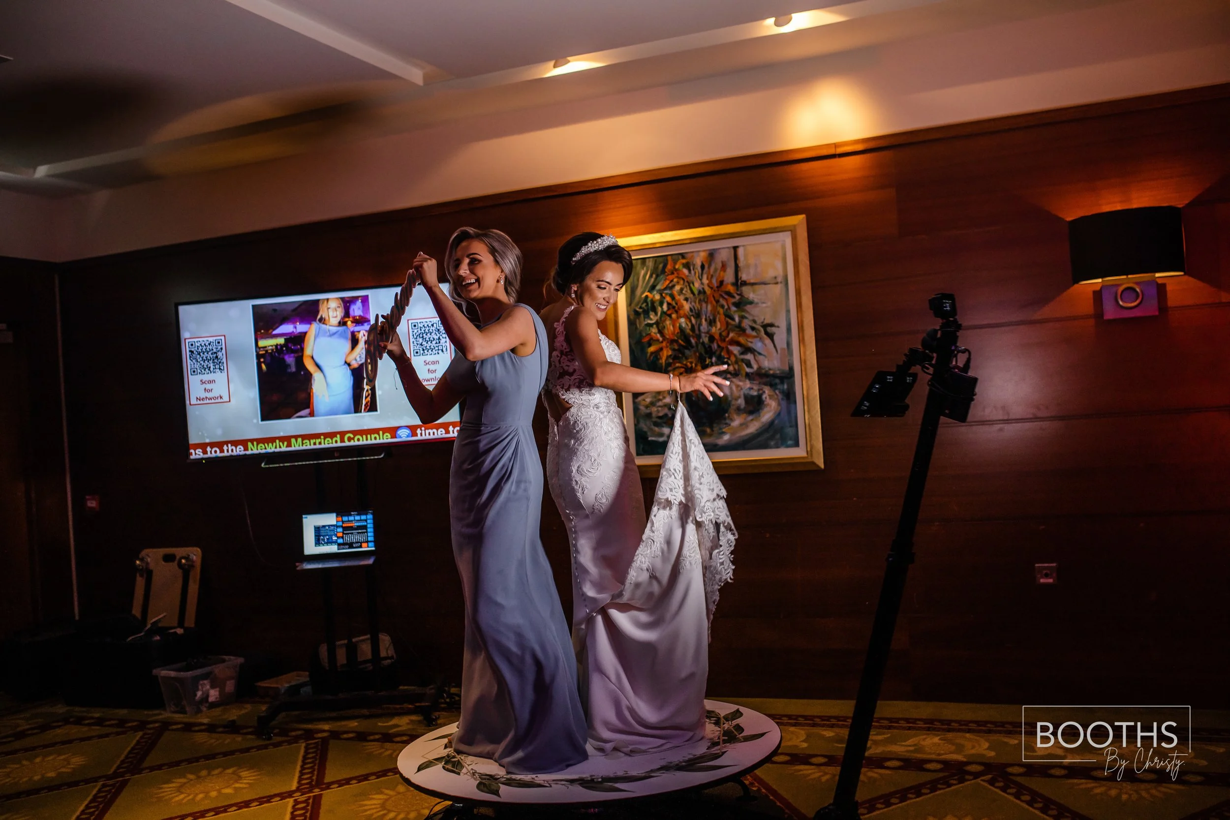 Bride and bridesmaid dancing on a 360-degree photo booth platform at a wedding reception.