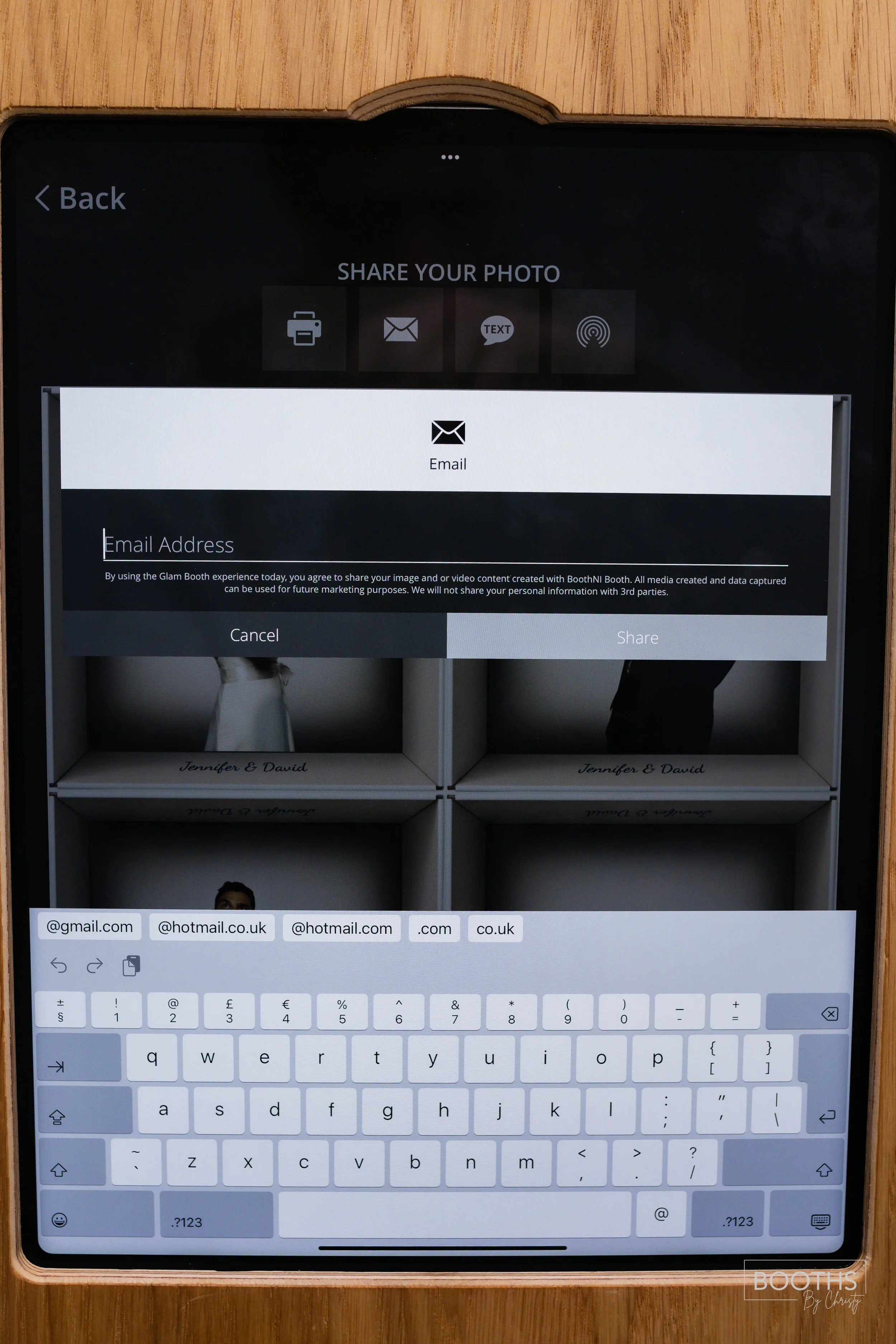 Tablet screen showing a photo-sharing app with a background image of small boxes labeled 'Jennifer & David' and a keyboard at the bottom for entering an email address.