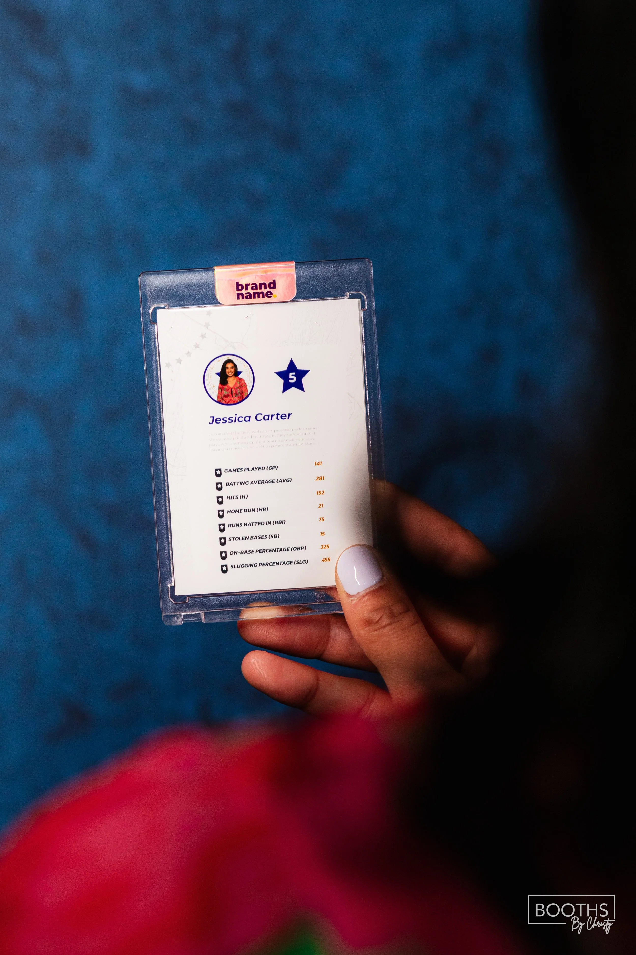 Close-up of a hand holding a sports card with statistics for Jessica Carter, including games played, batting average, hits, home runs, runs batted in, stolen bases, on-base percentage, and slugging percentage, against a blue background.