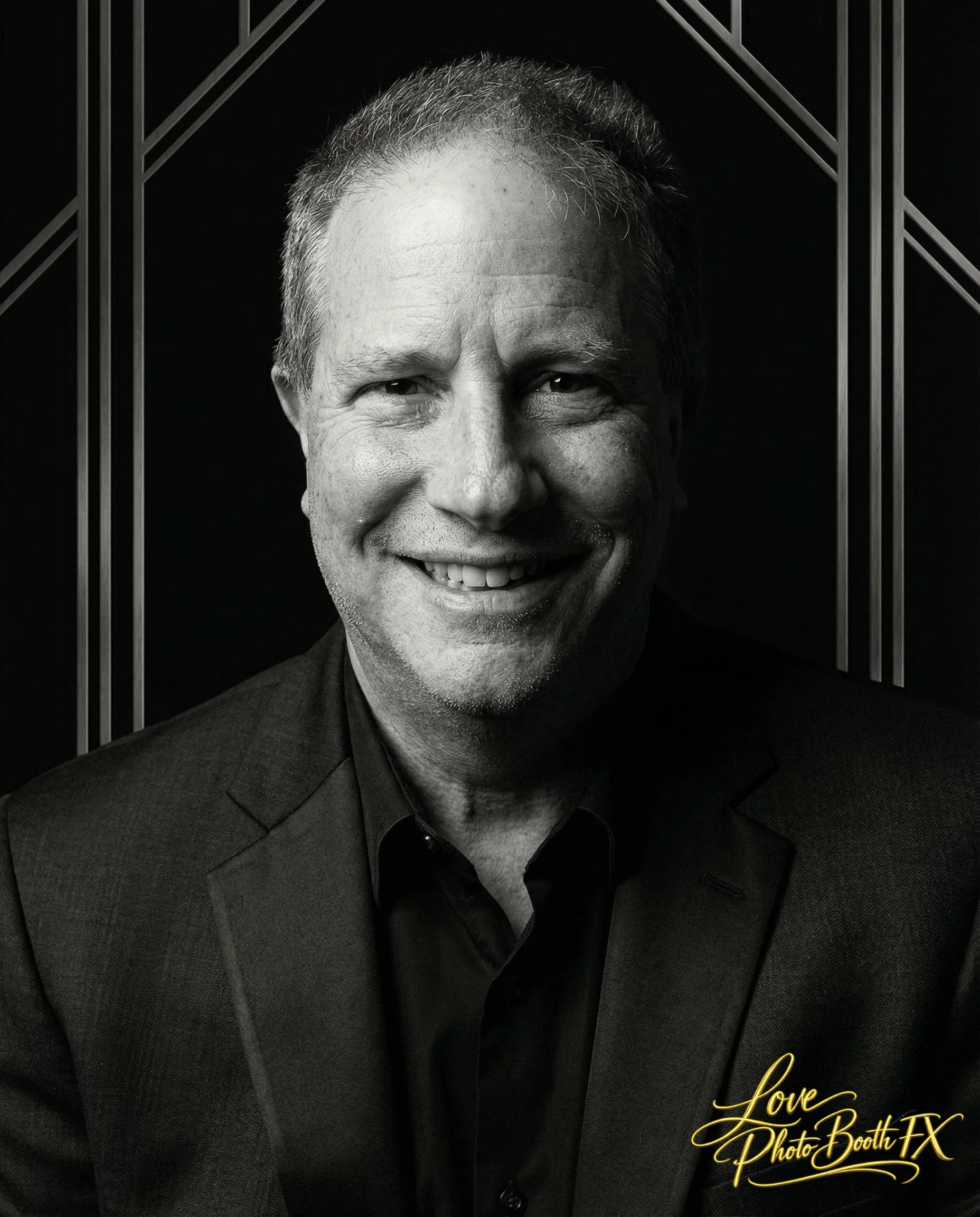 Black and white portrait of a smiling middle-aged man in a suit, background with geometric design, bottom right corner has gold text reading "Love Photo Booth FX".