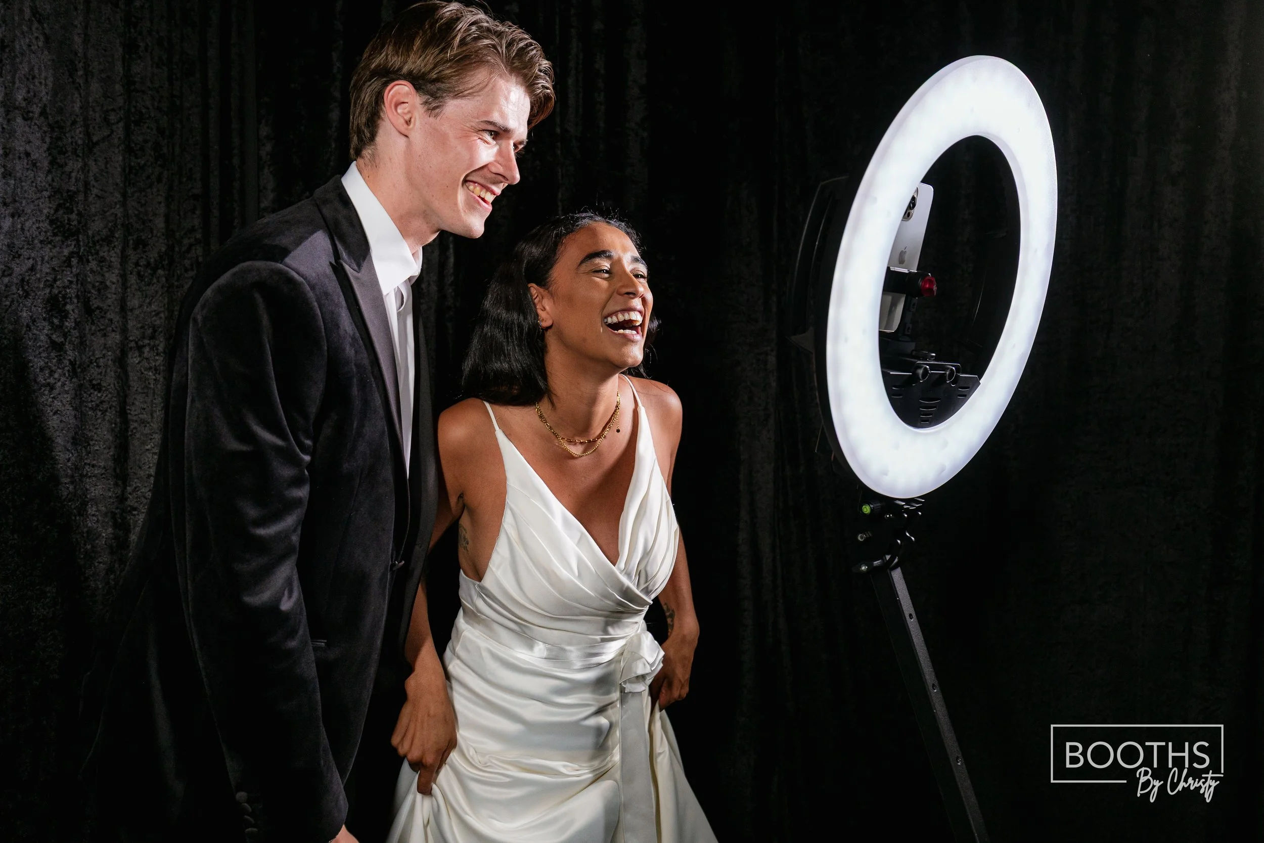 A man and woman in formal attire taking a photo together with a ring light.