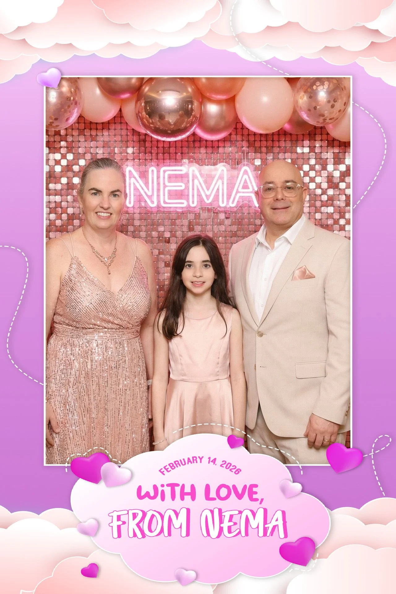 A family of three standing in front of a pink and rose gold backdrop with balloons and a neon sign that reads 'NEMA'. The family includes a woman in a pink sequin dress, a young girl in a light pink dress, and a man in a beige suit. There is a pink c