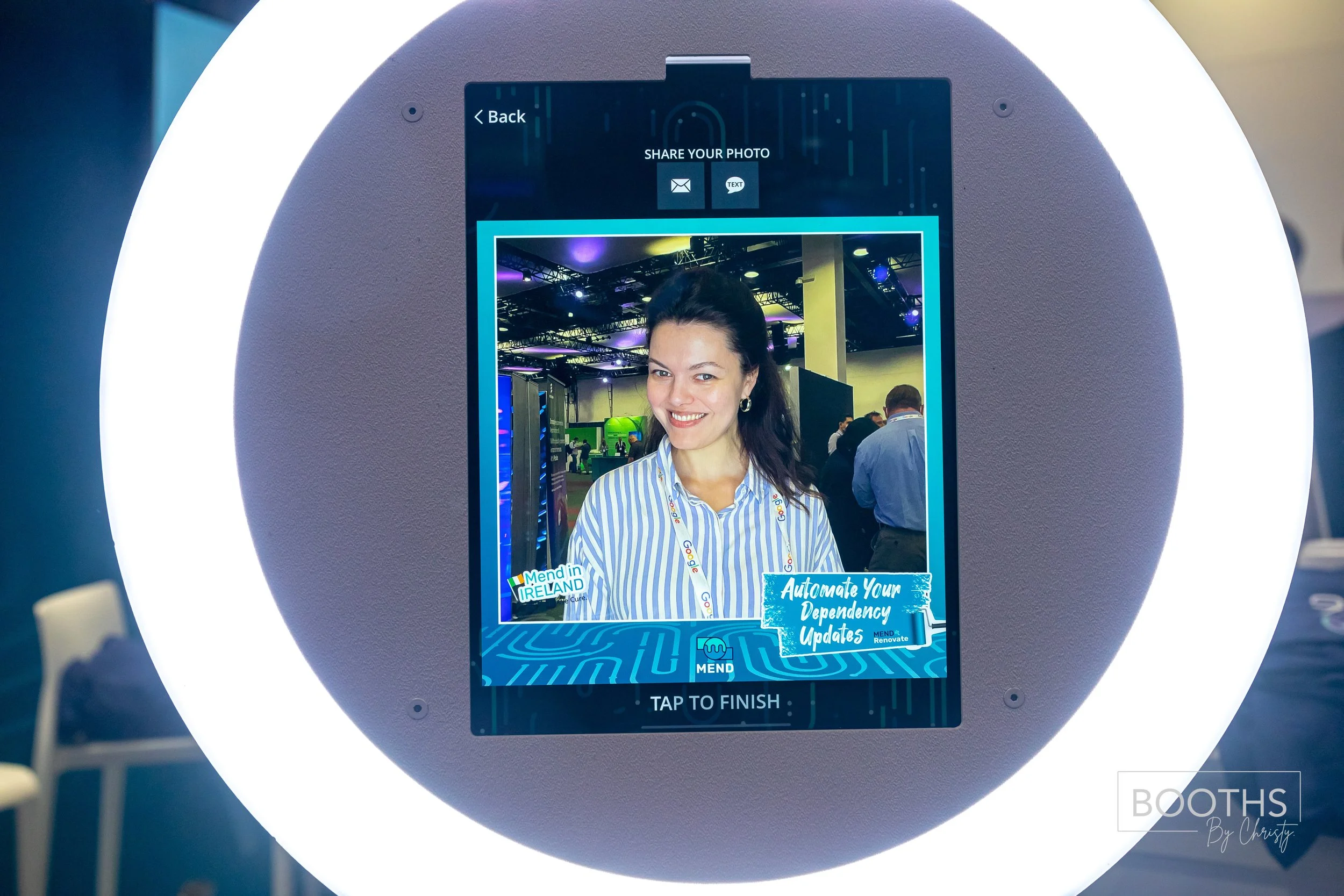 A woman is smiling on a digital photograph kiosk at a conference, with a sign promoting dependency updates and Ireland in the bottom left corner.