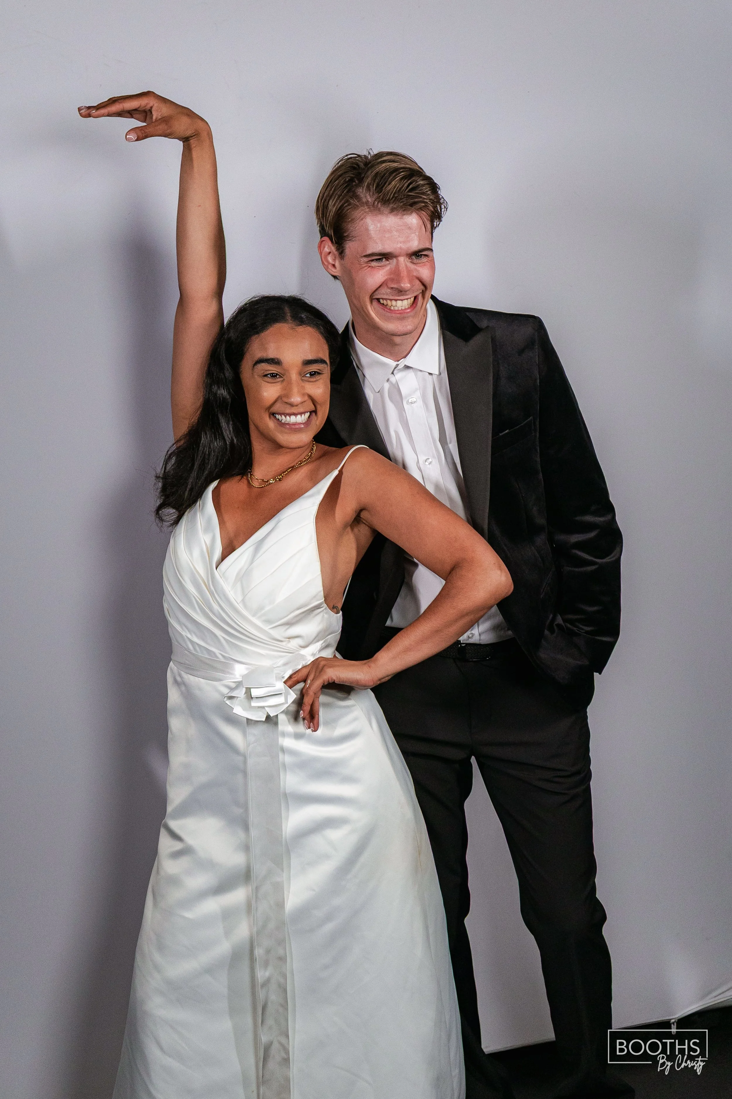 A woman in a white dress and a man in a black tuxedo posing together and smiling at the camera.