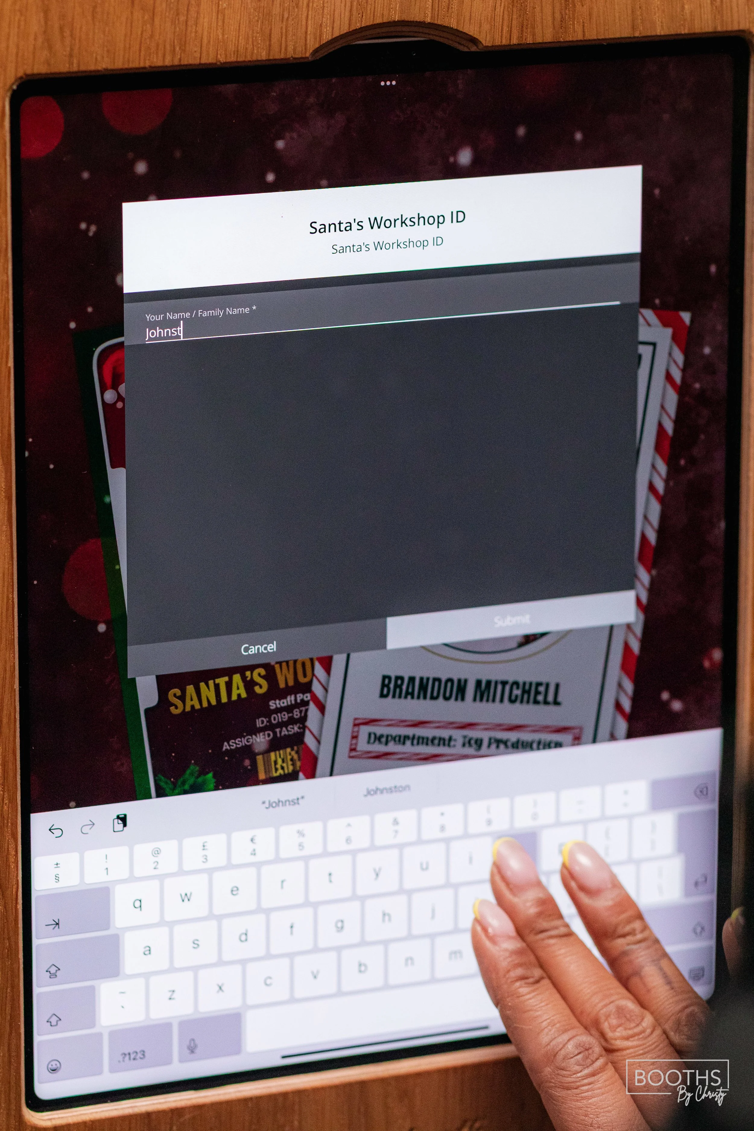 A person filling out a digital form for Santa's Workshop ID on an iPad, with holiday-themed cards visible in the background.