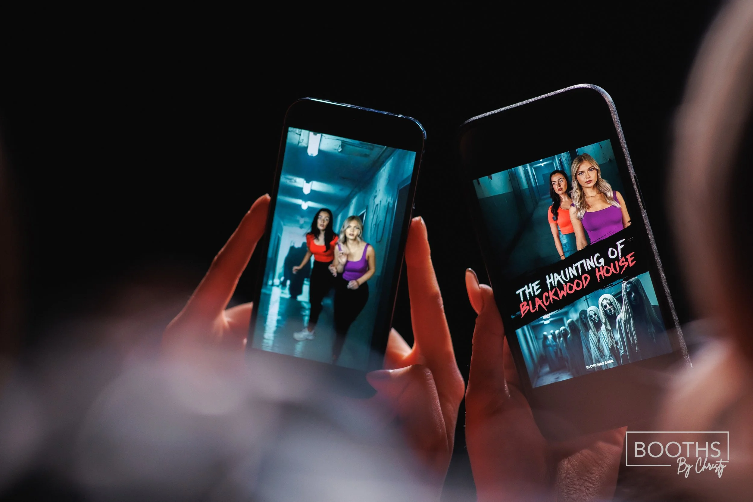 Two hands holding smartphones, one with a photo of two women walking in a hallway and the other displaying a movie poster for 'The Haunting of Blackwood House' with two women and creepy figures in the background.