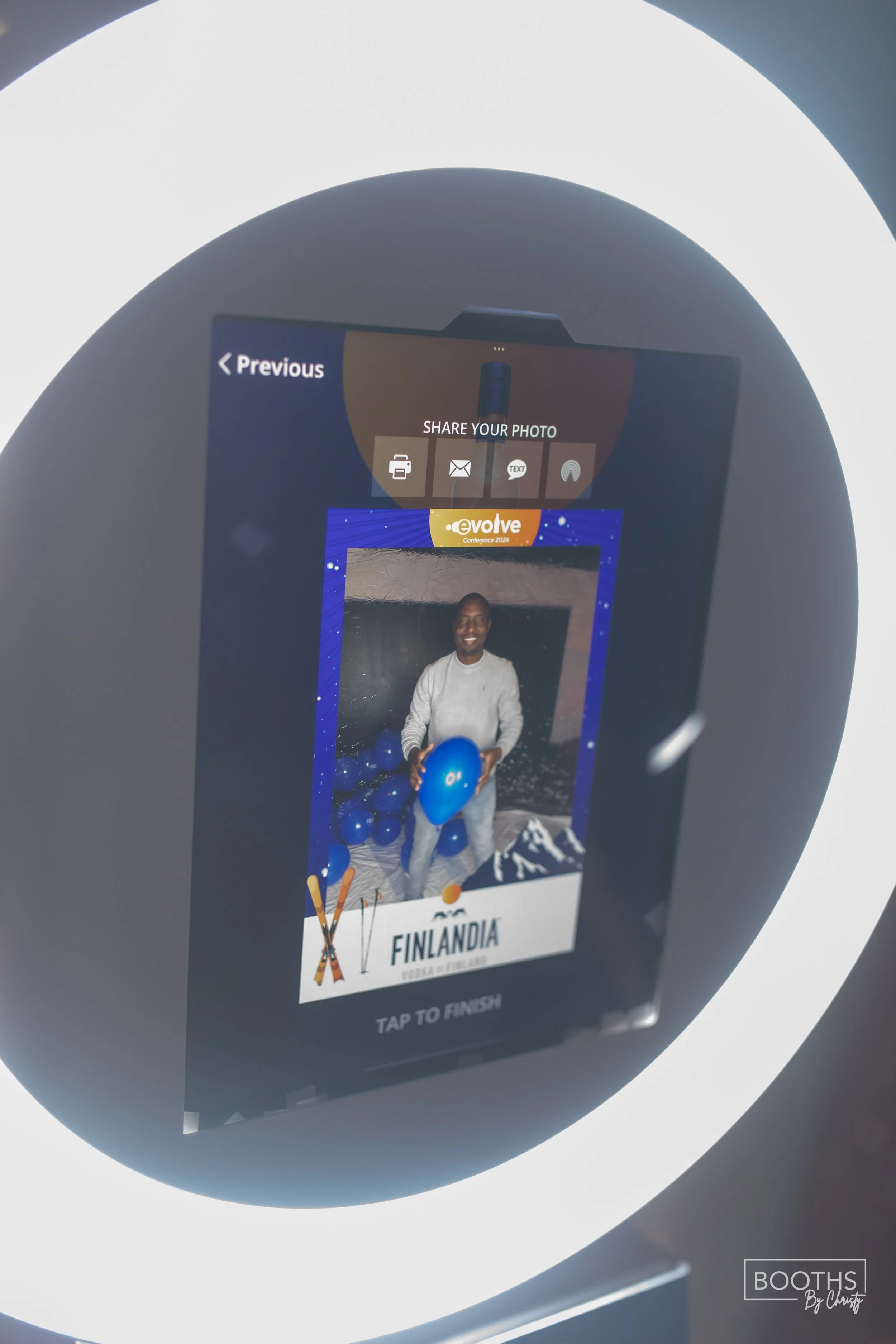 A person holding a blue balloon on a photo screen at a photo booth, with the word "Finlandia" and a mountain logo, indicating the image is from an event or conference.