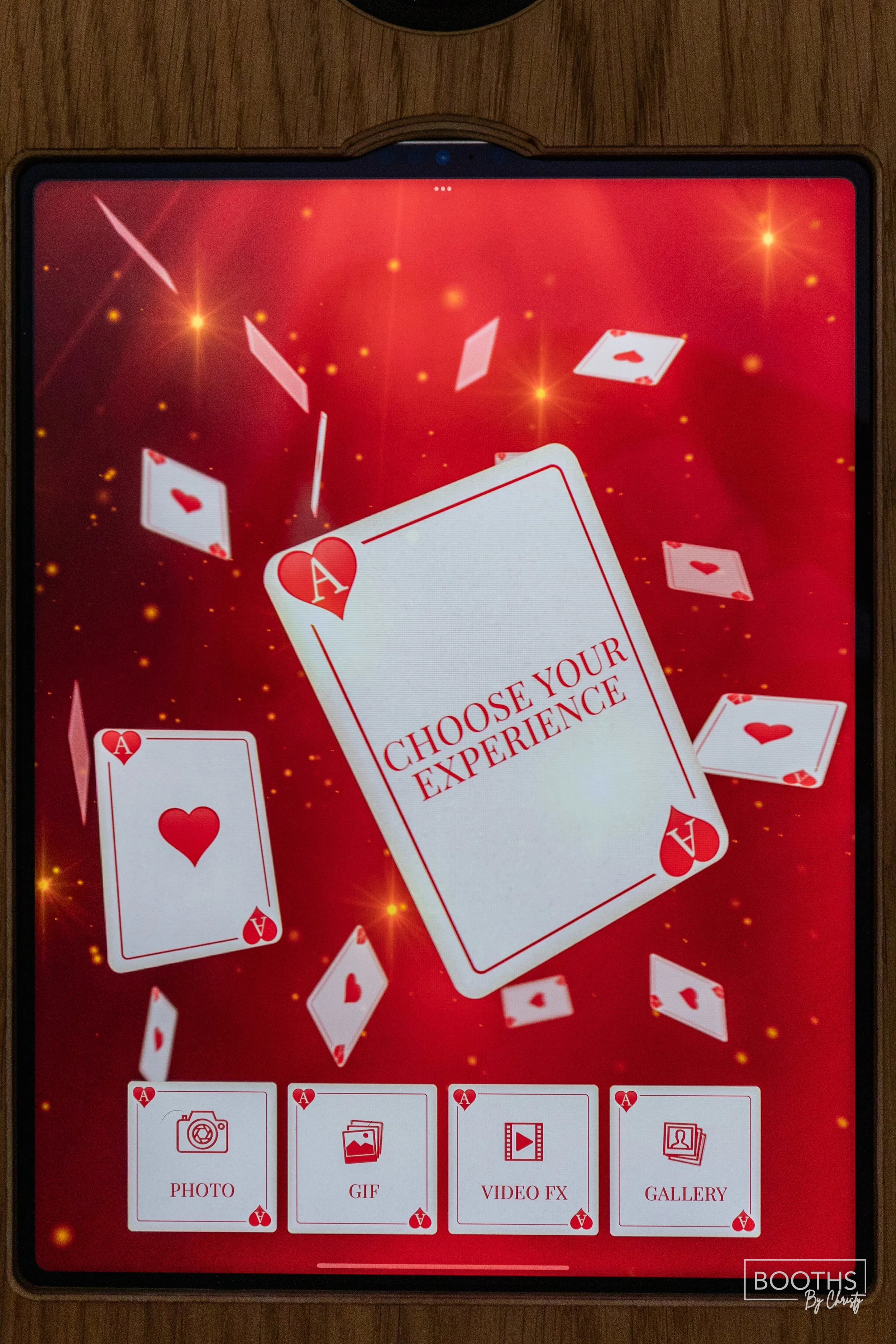 A digital card game app with a red background, floating playing cards with hearts and diamonds, and options at the bottom for PHOTO, GIF, VIDEO FX, and GALLERY, with a central card displaying the message "CHOOSE YOUR EXPERIENCE."