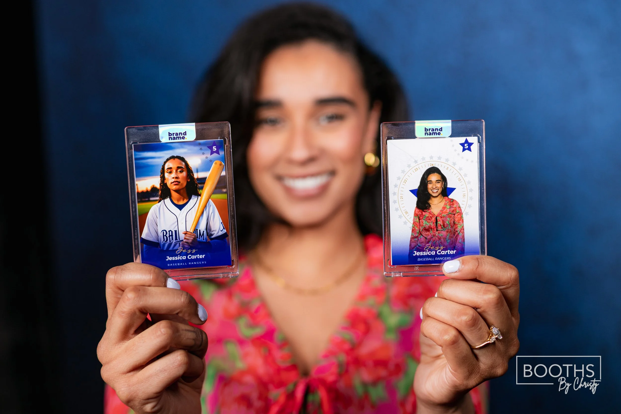 A woman holding two custom photo IDs of herself, one in a baseball uniform and the other in a floral top, smiling in front of a dark background.