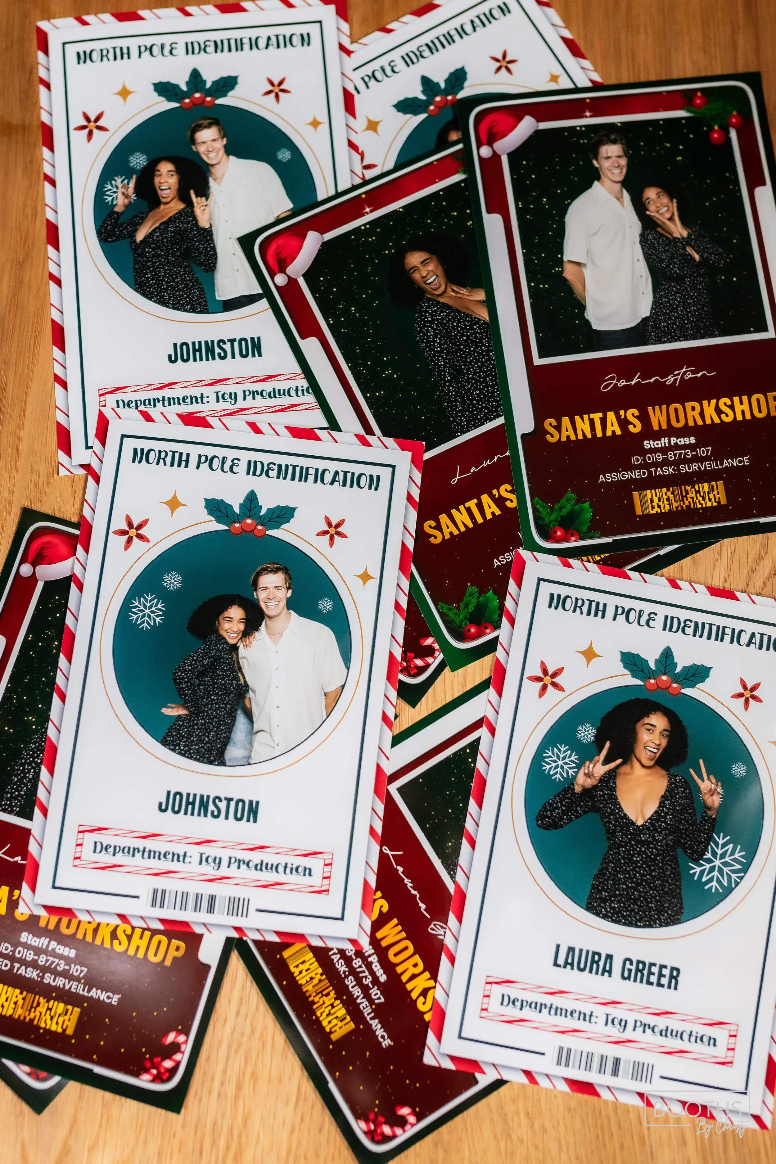 Multiple Christmas-themed North Pole identification cards for toy production department with photos of two people, including Santa's workshop staff pass, decorated with holly and snowflakes, laid on a wooden surface.