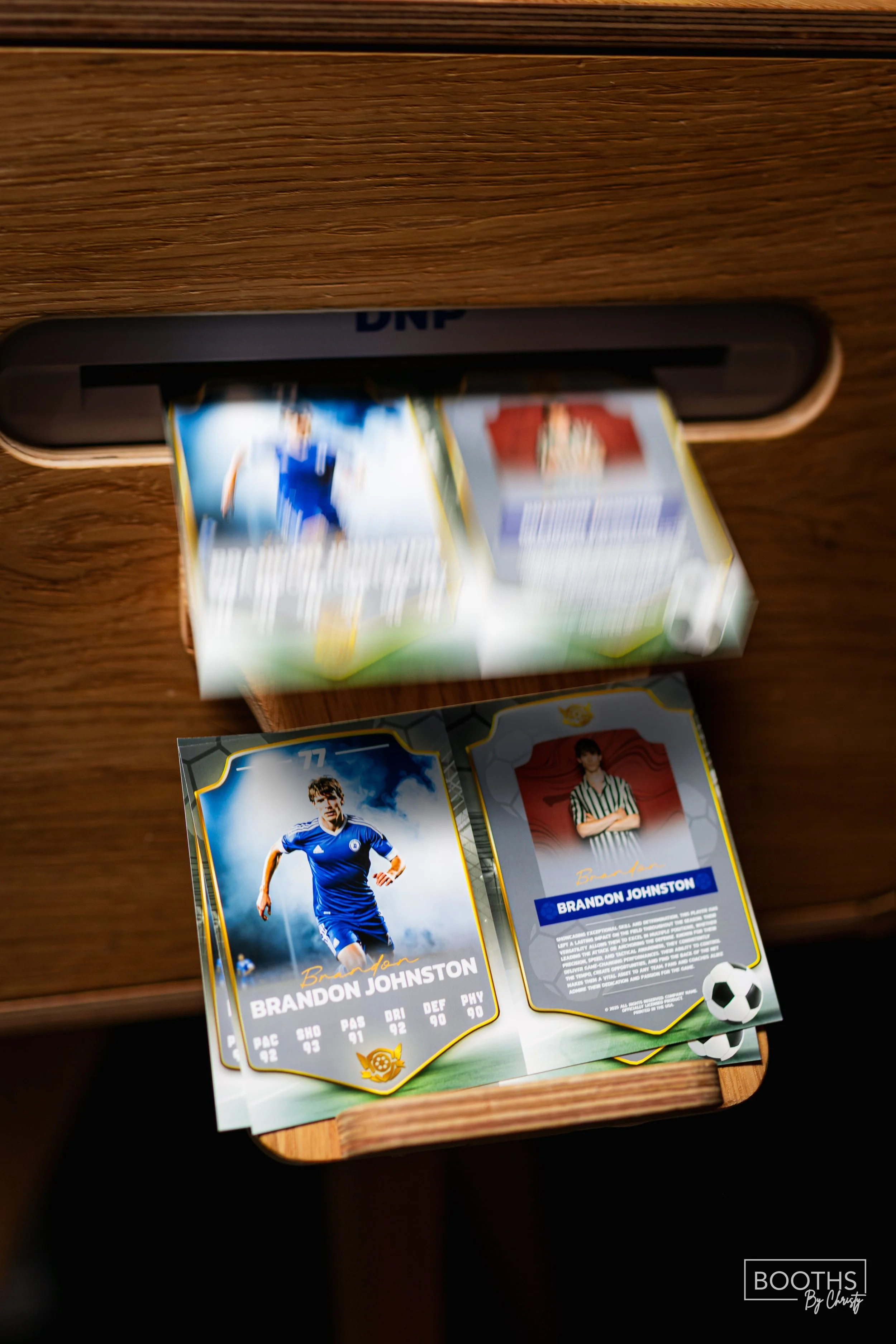 Surprised focus on a cardboard football trading card of Brandon Johnston, showing his picture, stats, and a soccer ball graphic, on a wooden surface with a blurred box of trading cards in the background.