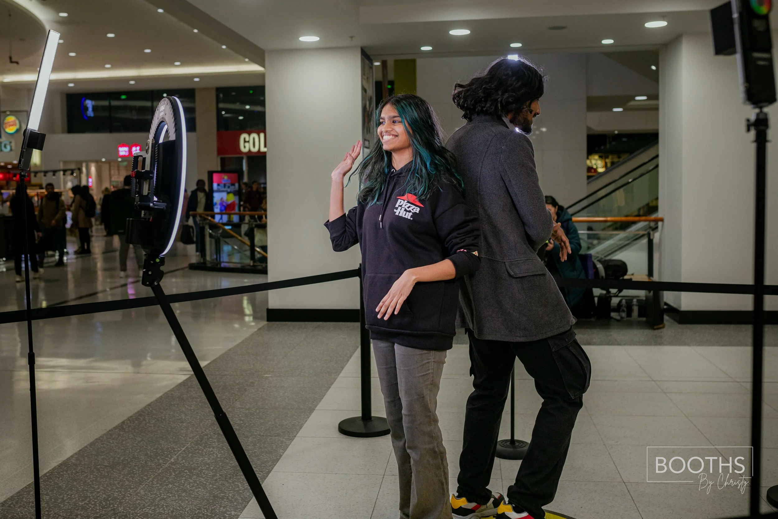 Two people standing back-to-back inside a shopping mall with photo booth setup.