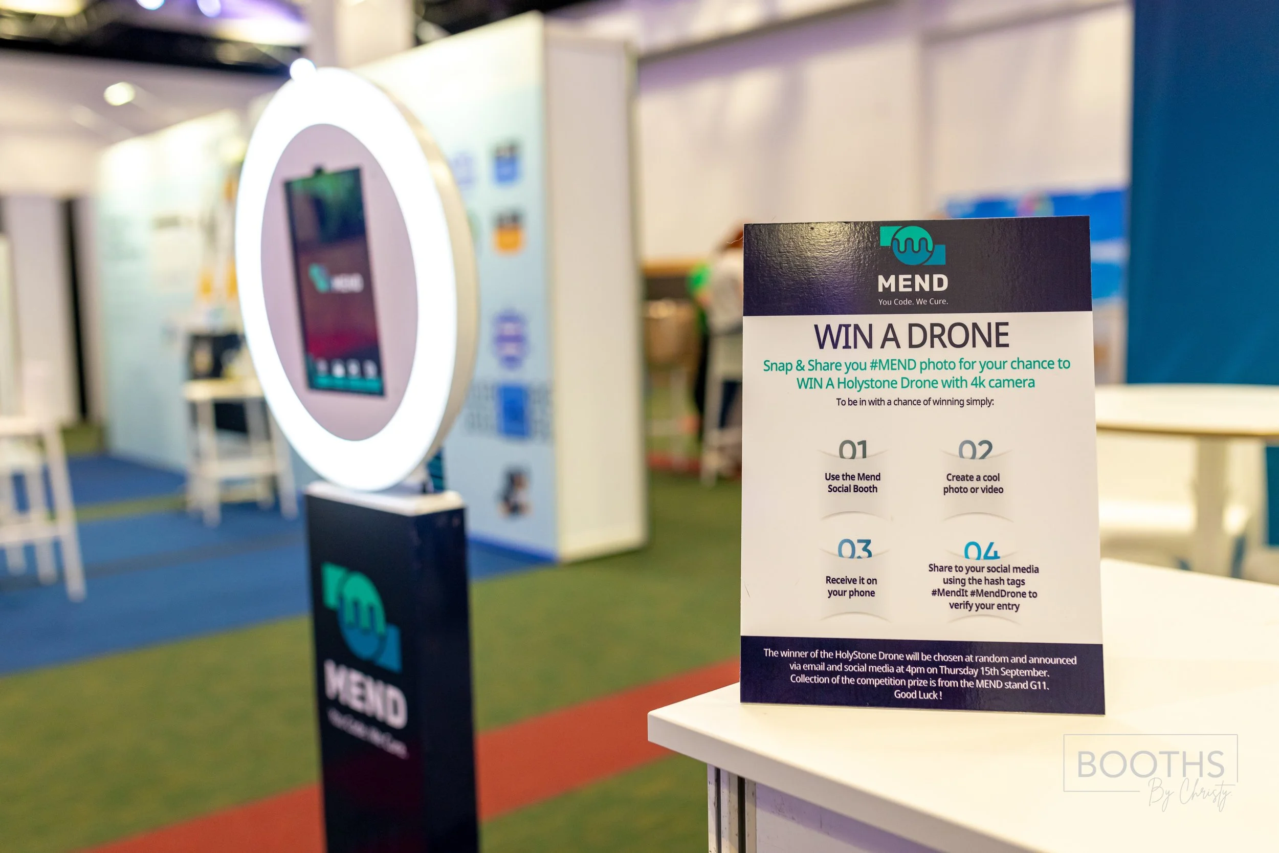 Sign promoting a drone giveaway contest at an indoor event, with a photo booth in the background.