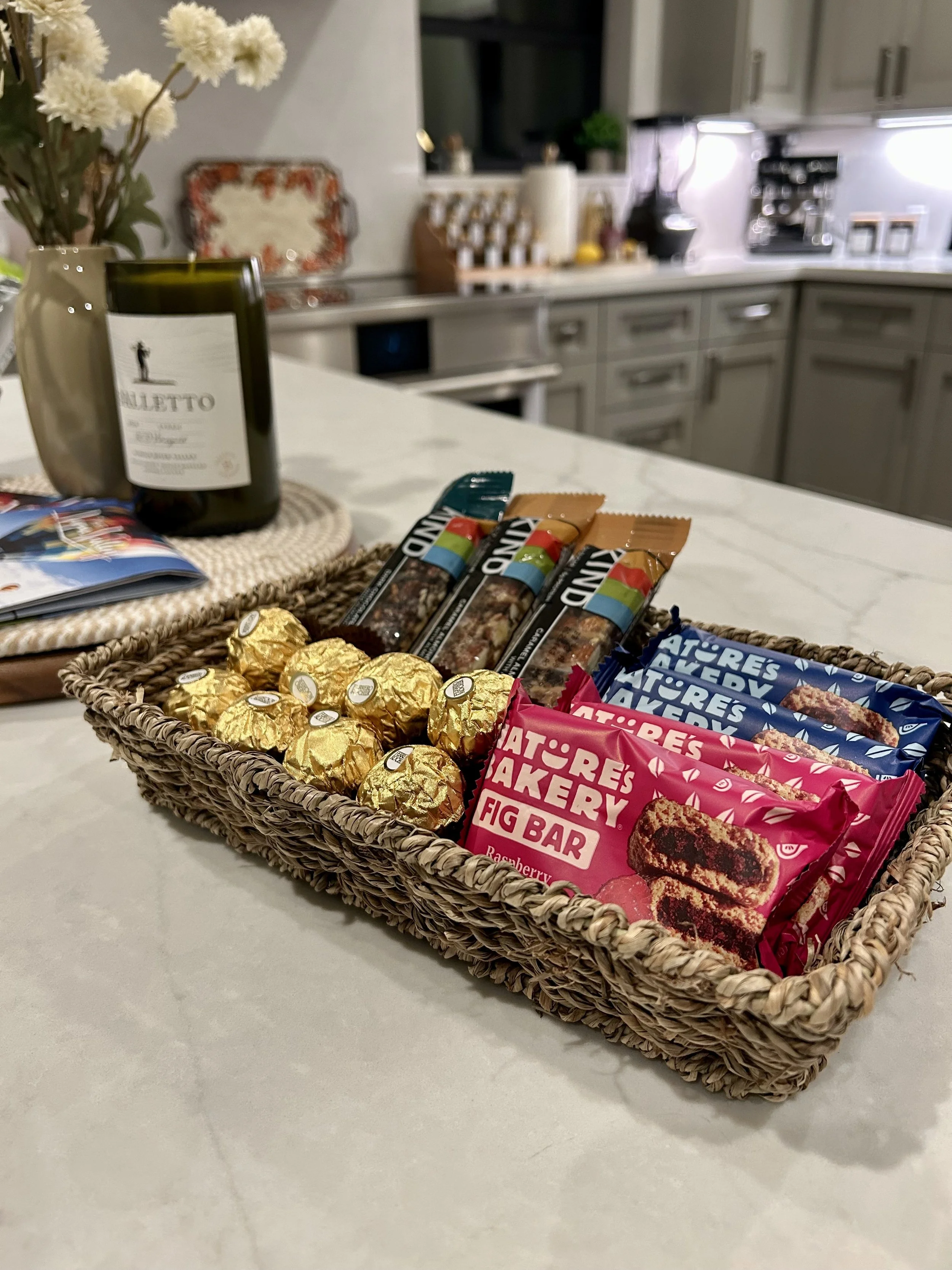 Bakery snack basket with chocolate bars, fig bars, and golden foil-wrapped chocolates on kitchen counter.