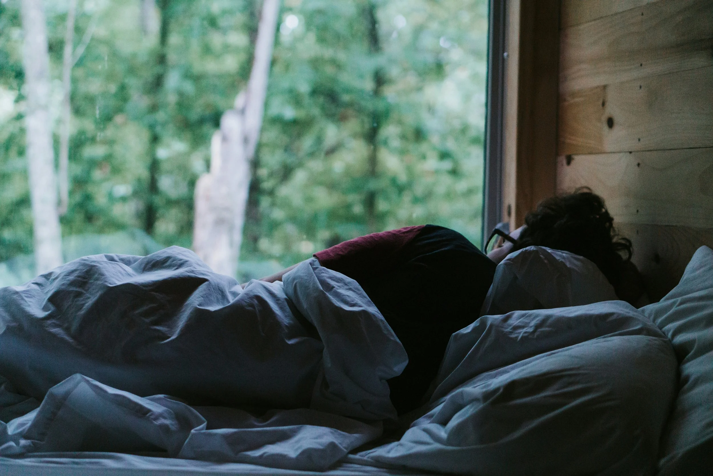 person laying in bed facing window to the woods